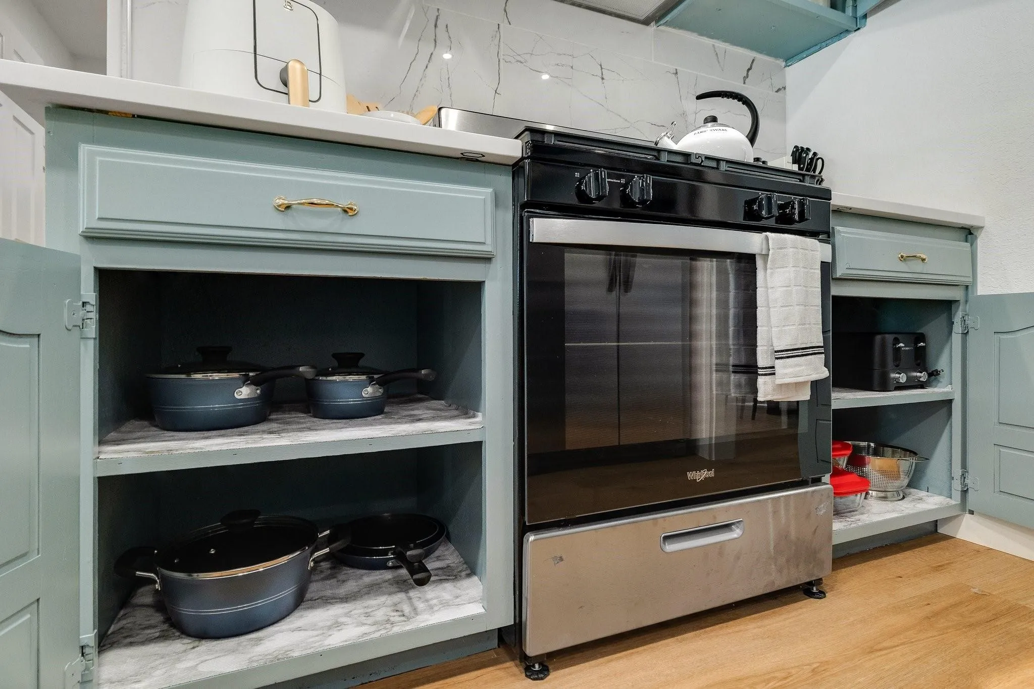 Kitchenette featuring a black and stainless steel range, light-toned cabinetry, light-toned countertops, and wood-finish flooring
