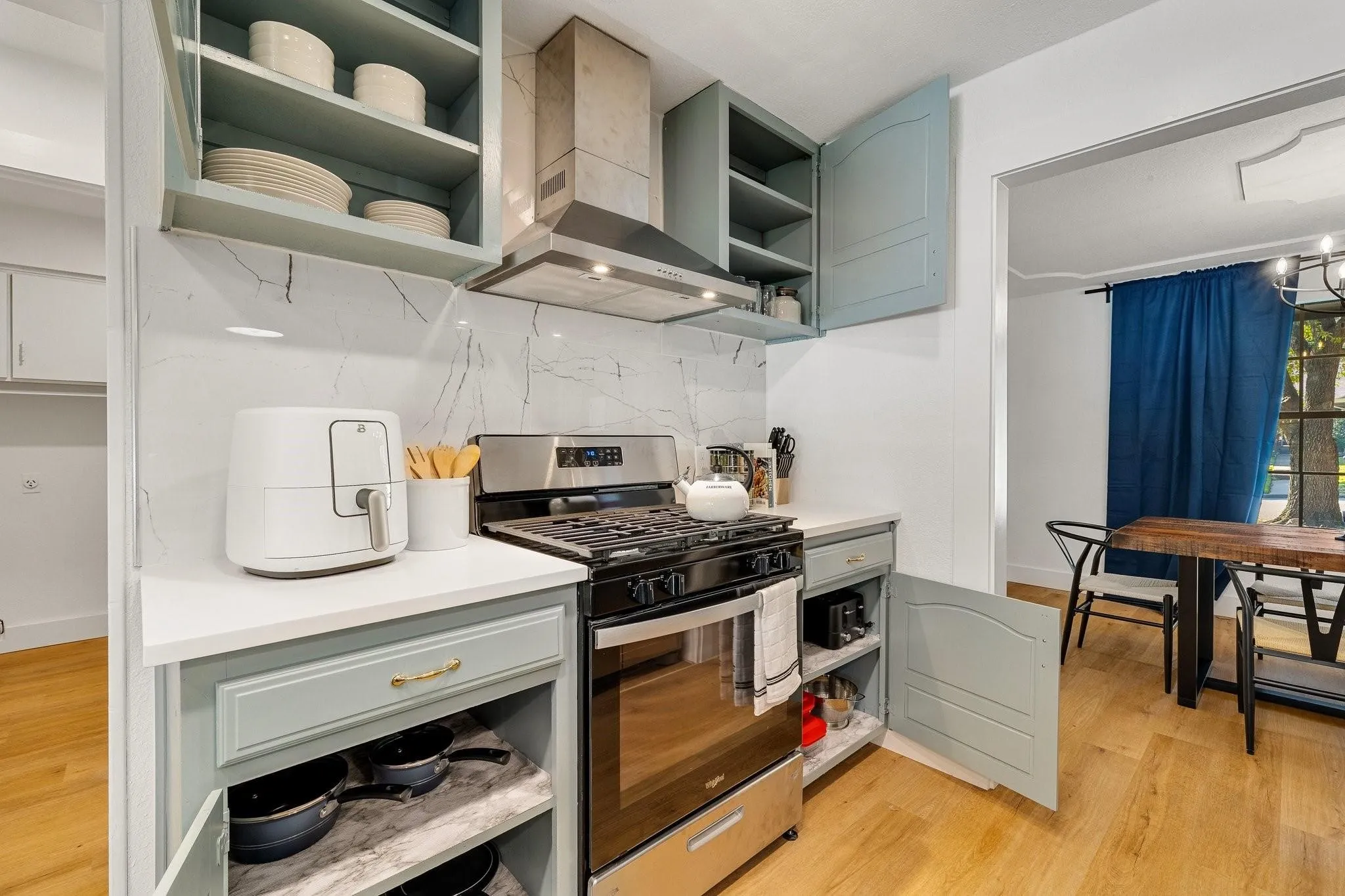 Stainless steel range with coordinating hood, marble-look backsplash, light-toned wood-finish flooring, and light blue cabinetry