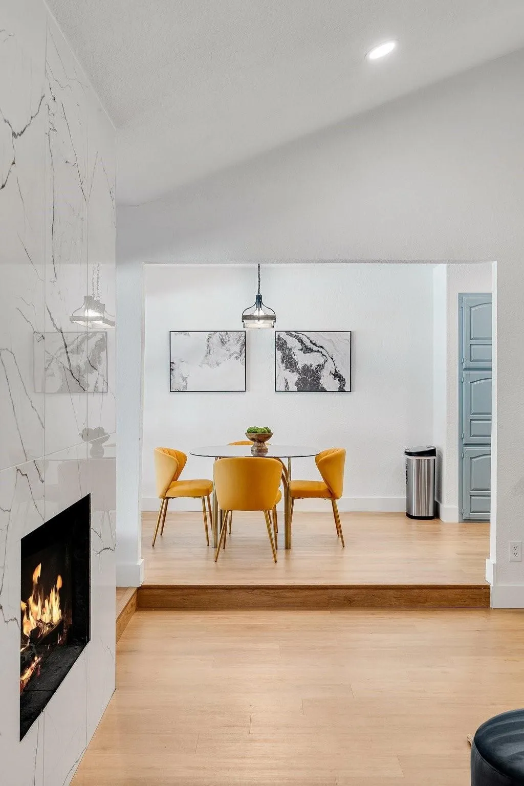 Vaulted ceiling with recessed lighting, linear fireplace with a marble-look surround, wood-finish flooring, and a dining area with a pendant light fixture