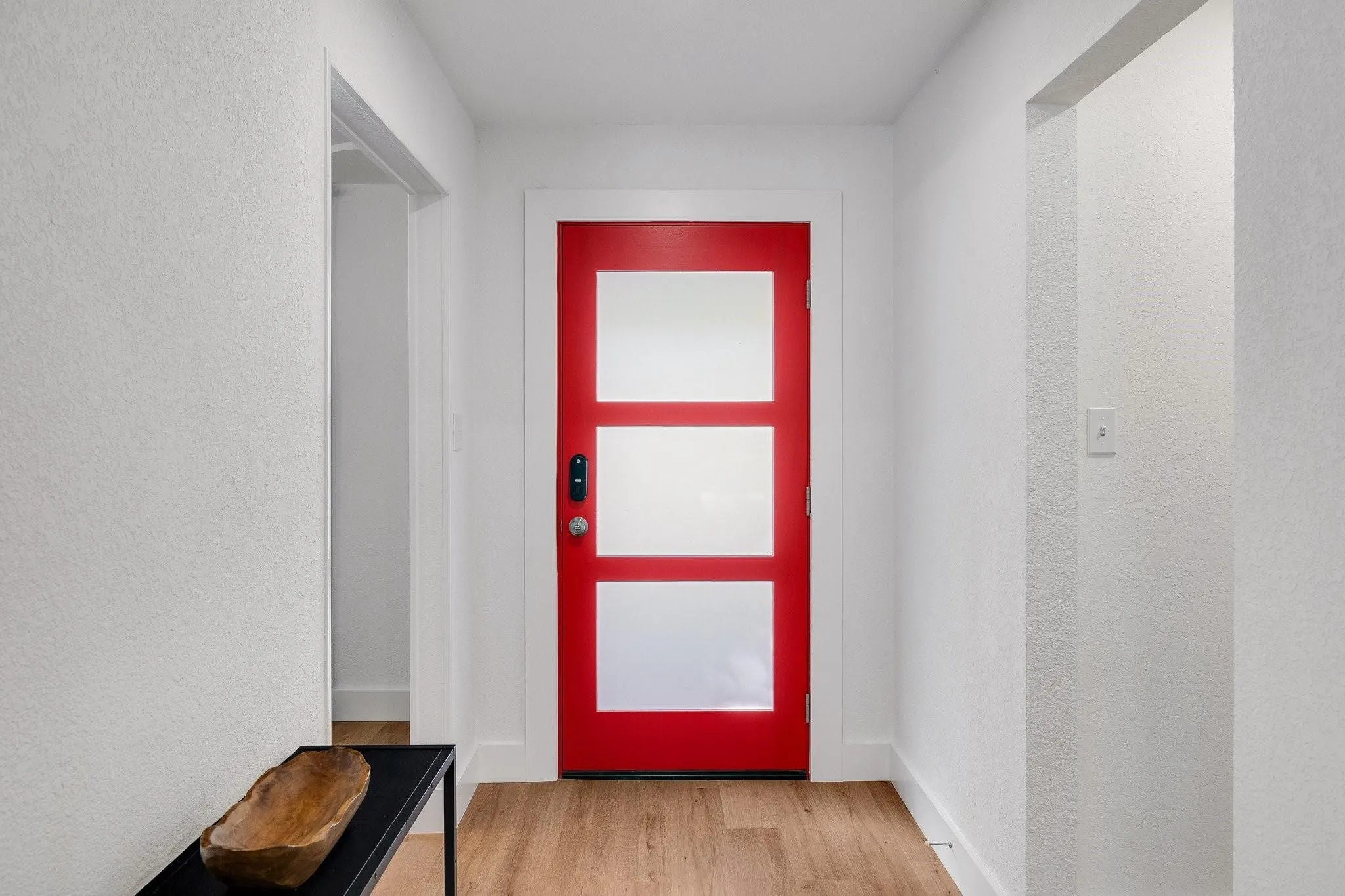 Red entry door with frosted panels, wood-finish flooring, white walls, and bright white trim