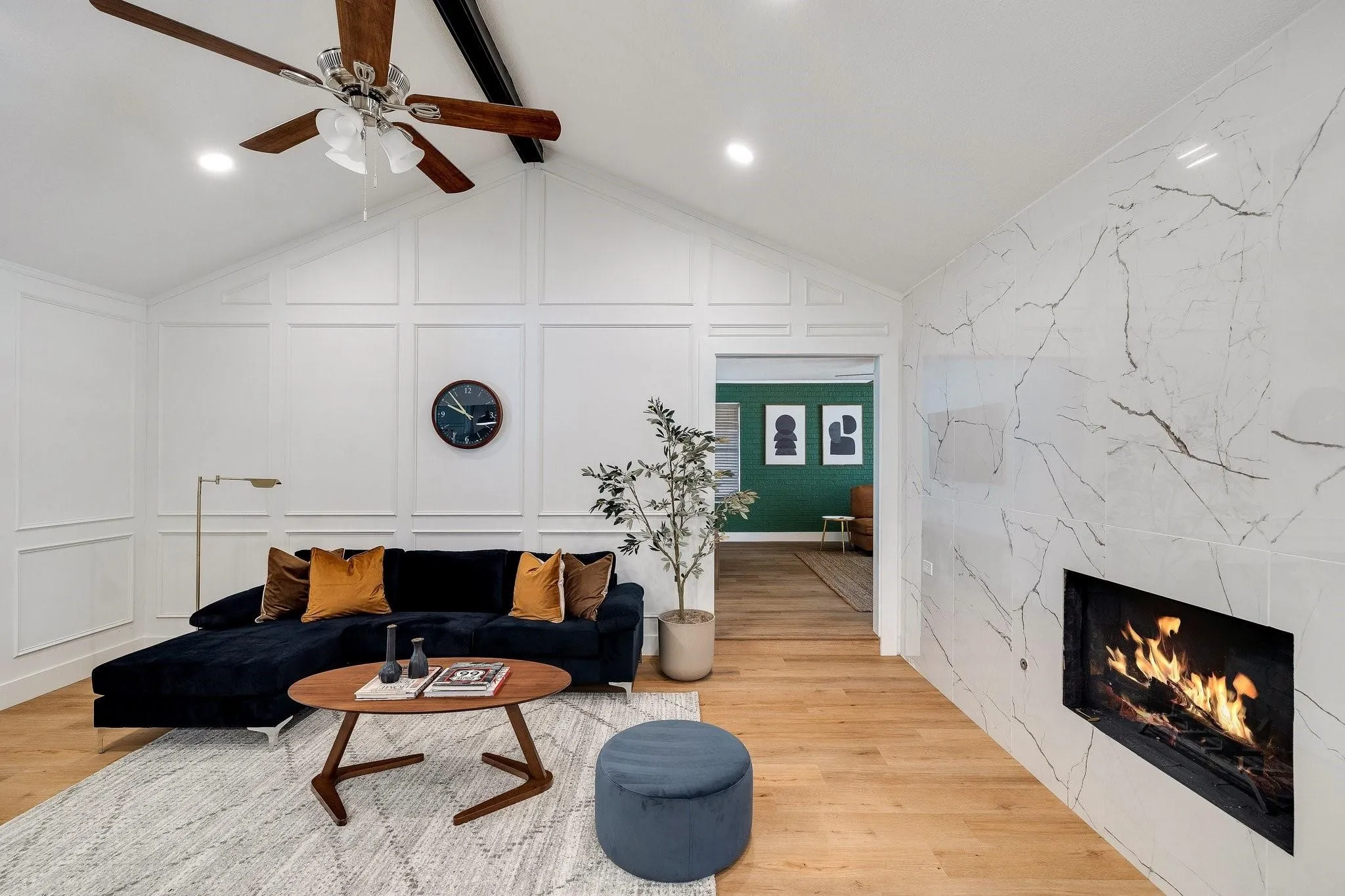 Vaulted ceiling with exposed beam, wood-finish flooring, accent wall paneling, recessed lighting, and a linear fireplace with a stone surround