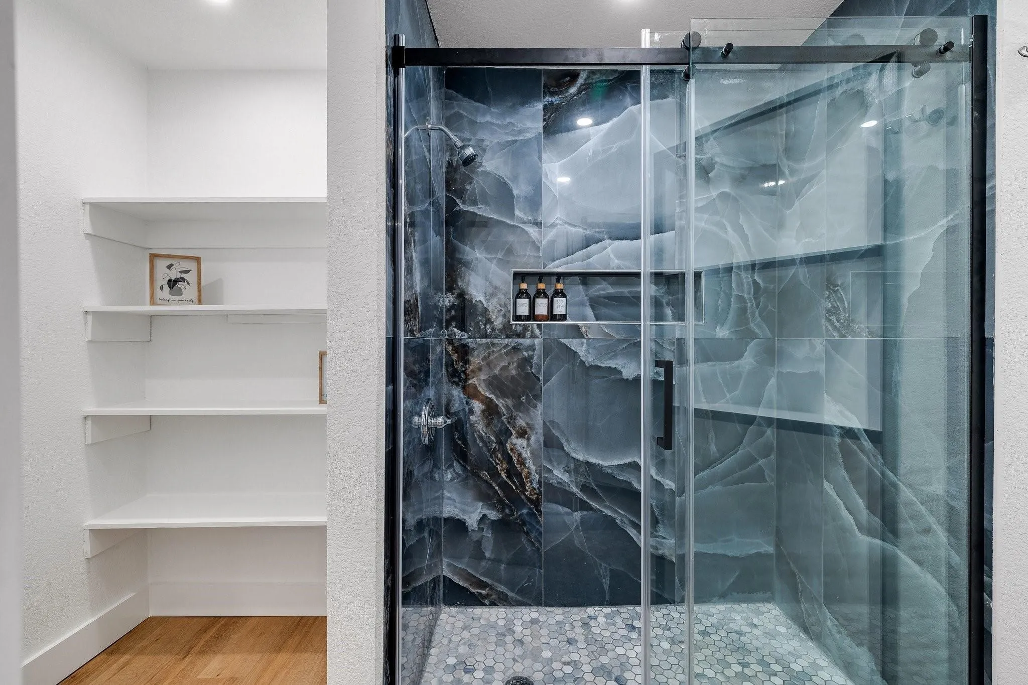 Sliding glass shower enclosure with dark-toned, large-format tile surround and hexagonal mosaic tile flooring