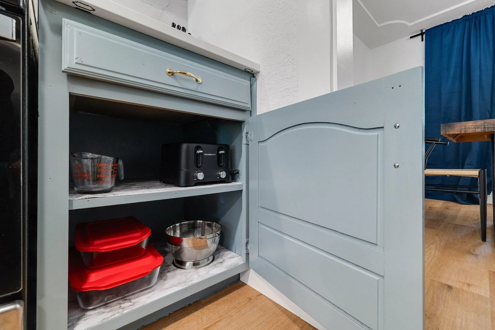 Cabinetry with a light blue finish, a gold-tone drawer pull, open shelving, and a solid wood-finish floor