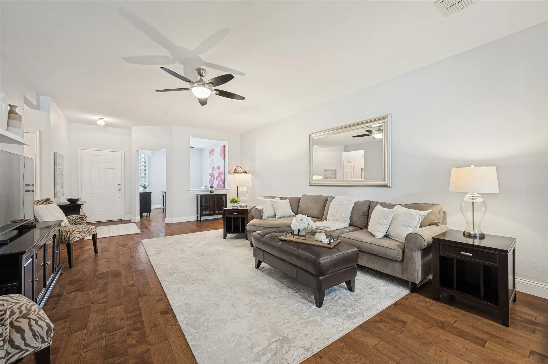 Spacious living area featuring wood-finish flooring, a ceiling fan with integrated lighting, and a white paneled entry door