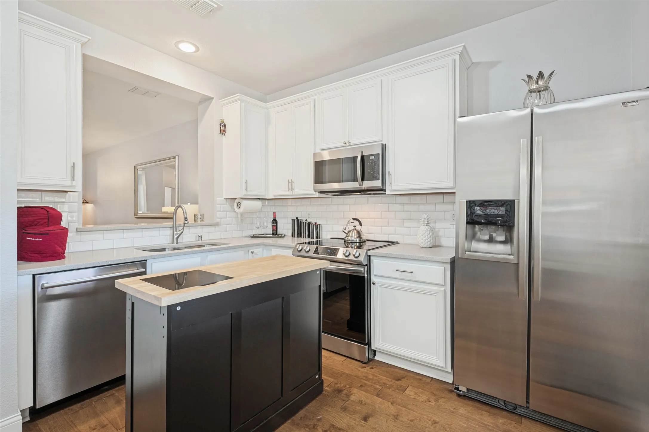 Modern kitchen featuring stainless steel appliances, white cabinetry, a white subway tile backsplash, and wood-finish flooring