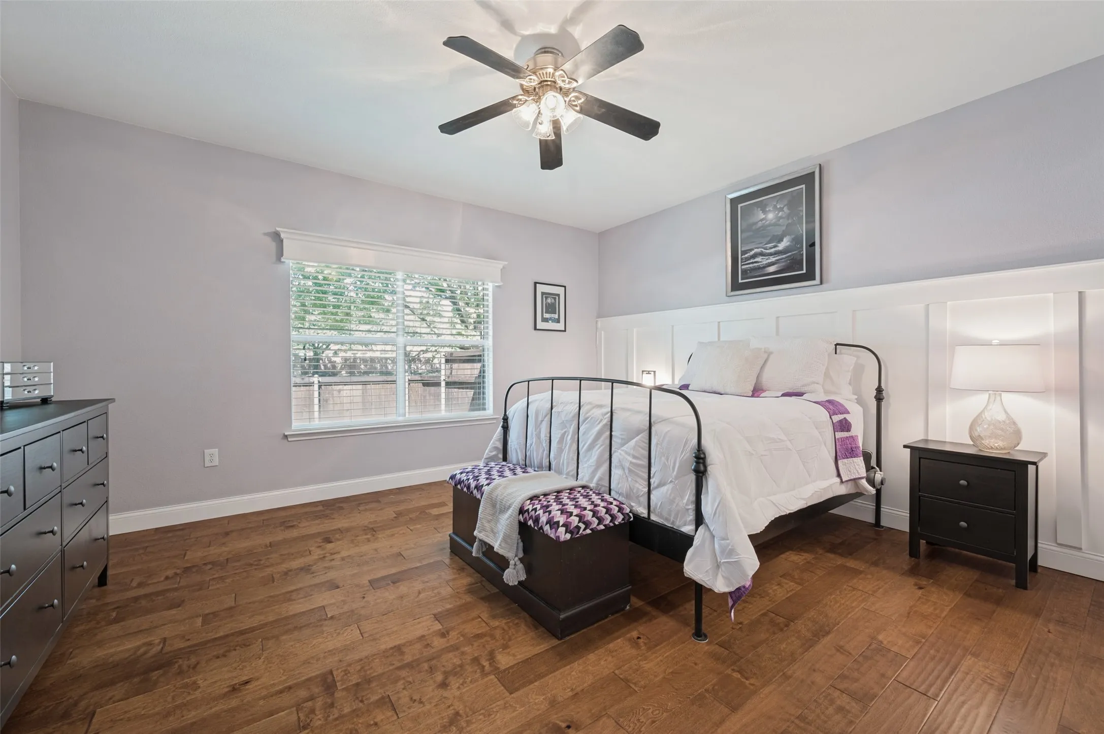 Wood-finish flooring, ceiling fan with integrated lighting, window with blinds, and white wainscoting
