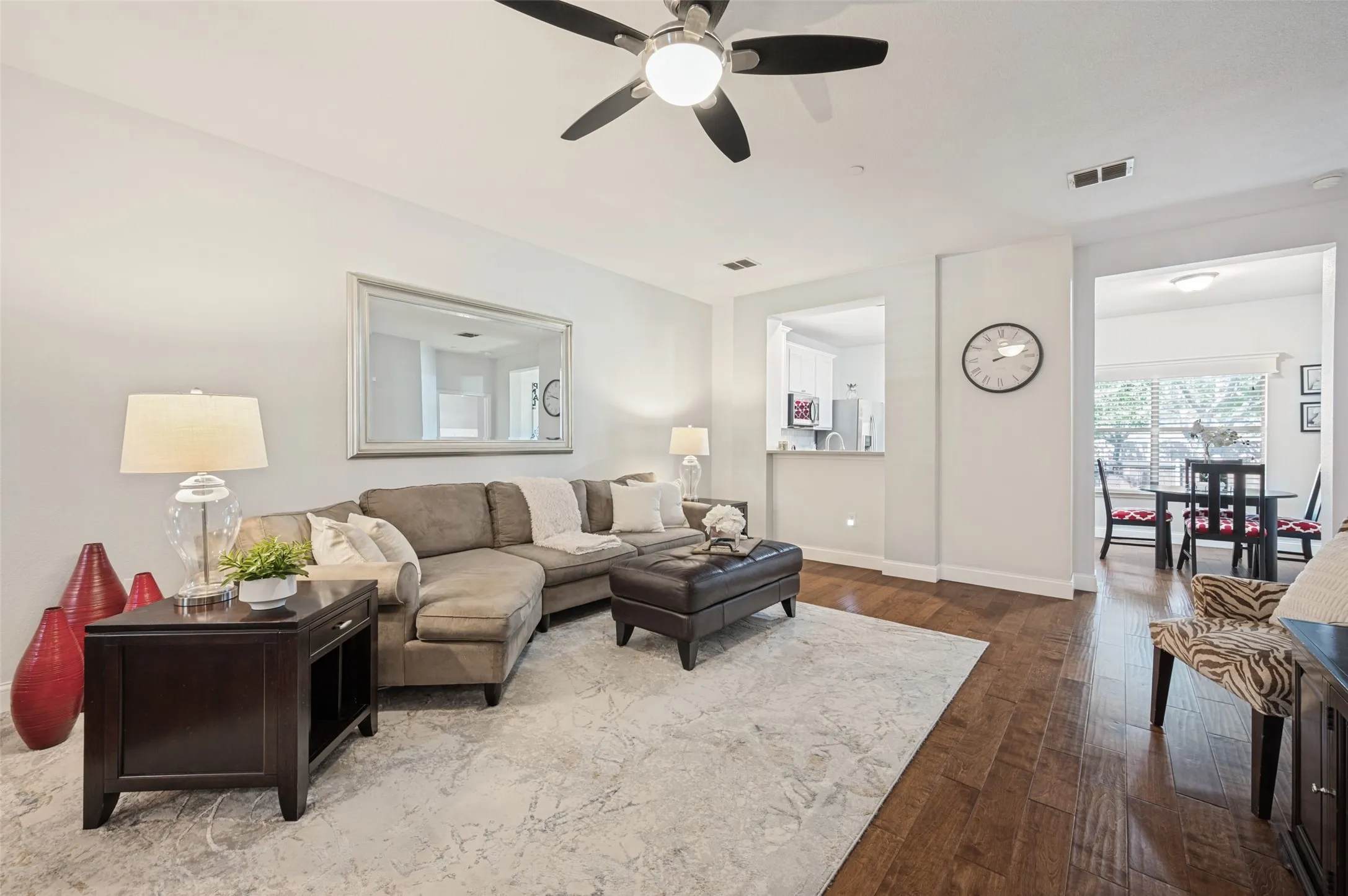 Wood-finish flooring, a ceiling fan with integrated lighting, and a pass-through window to the kitchen