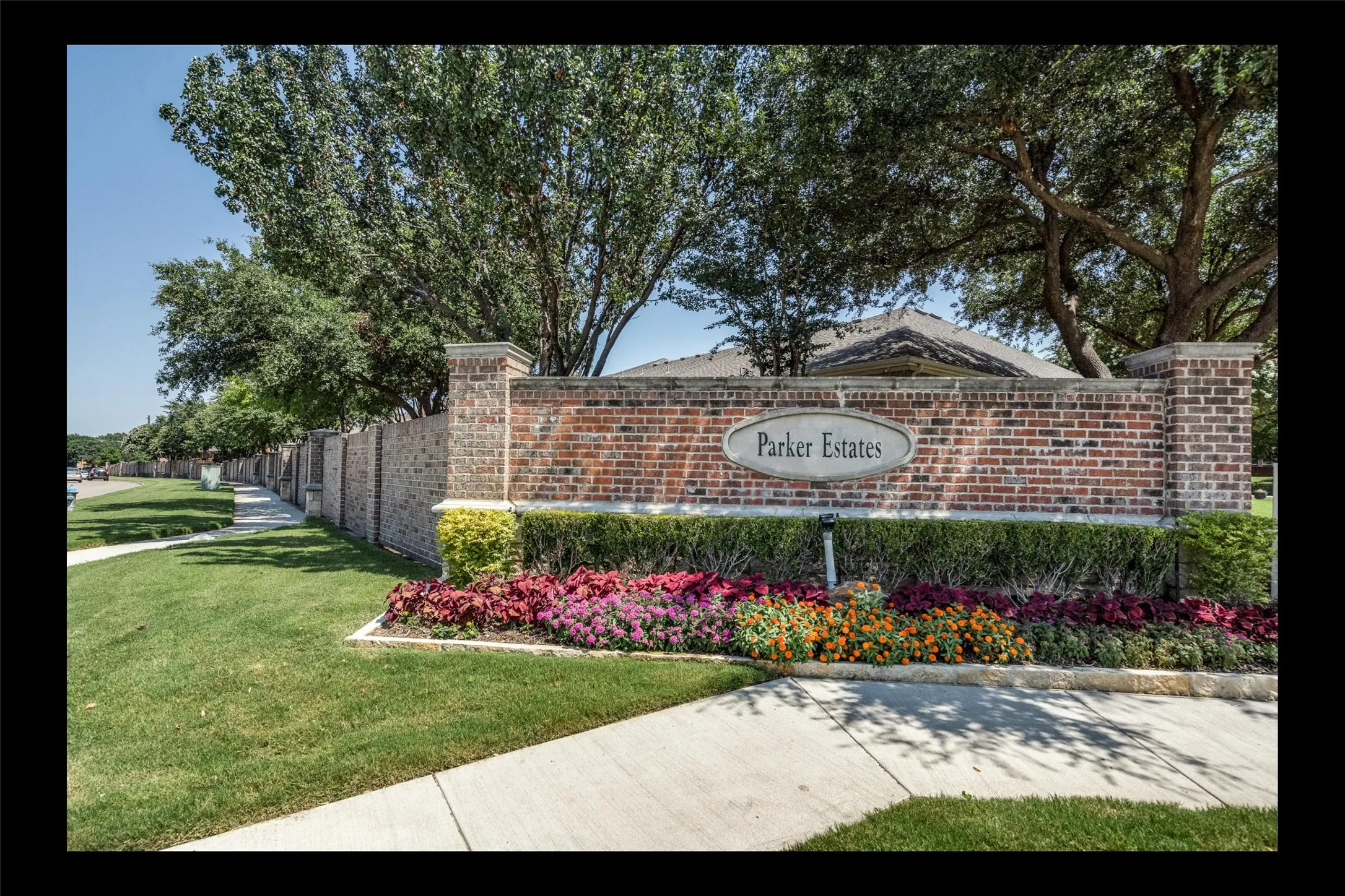 Brick entry wall with a "Parker Estates" sign, flanked by manicured shrubbery and colorful planted flowers