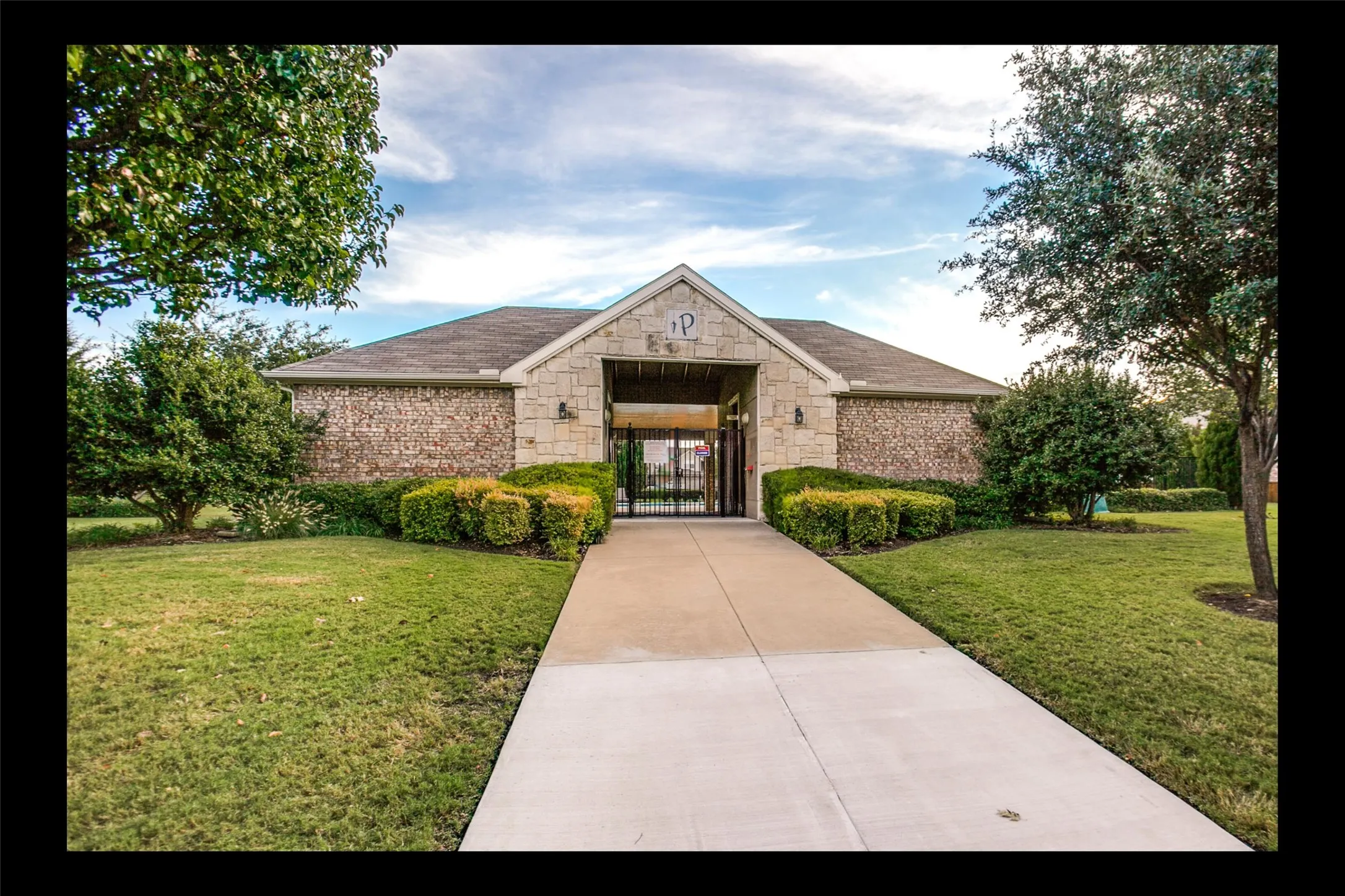 Stone and brick exterior building with a shingle roof and a concrete walkway