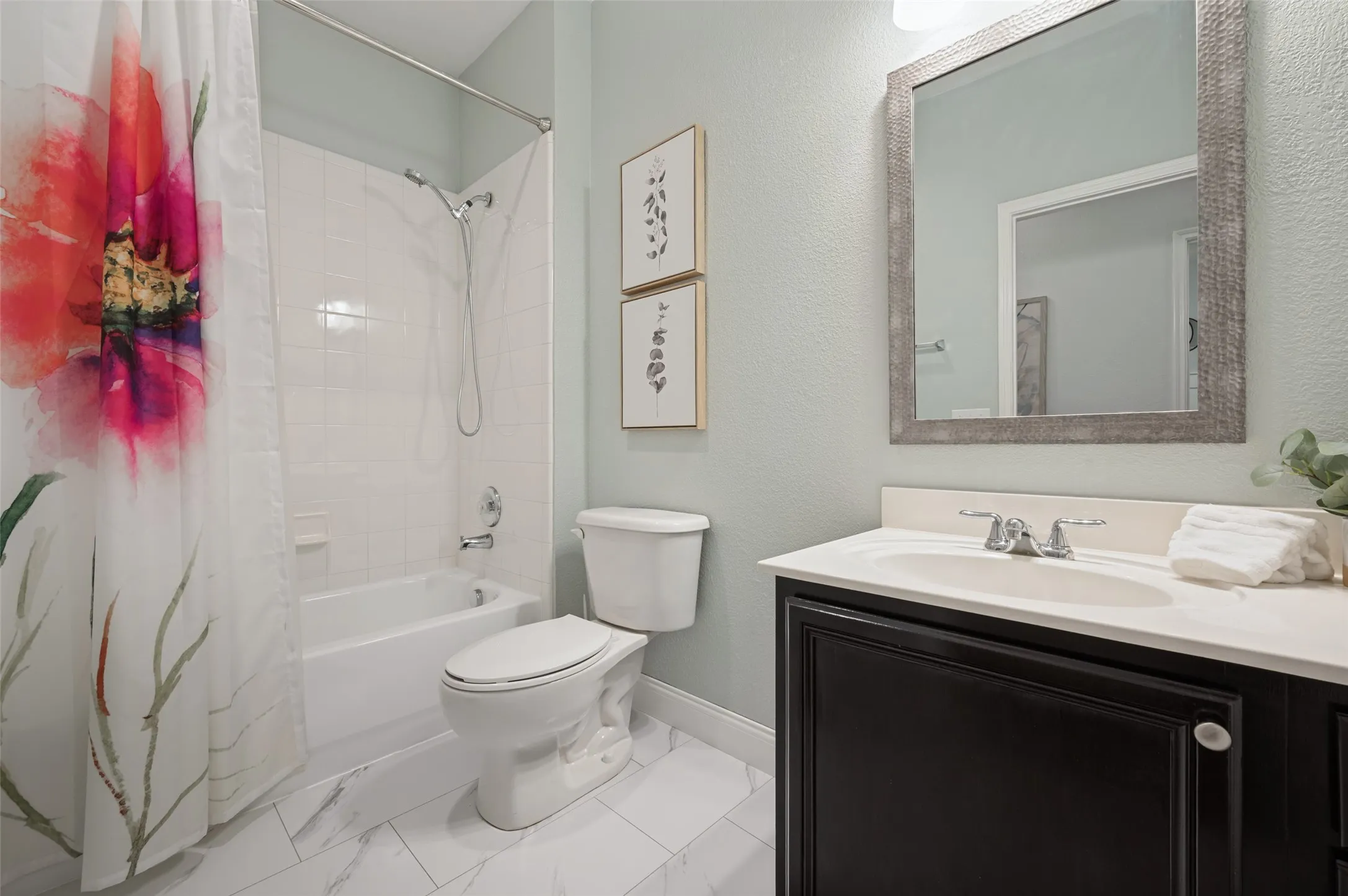 White ceramic tile bathtub with shower fixture, dark wood-finish vanity with white countertop, white undermount sink, and chrome faucet