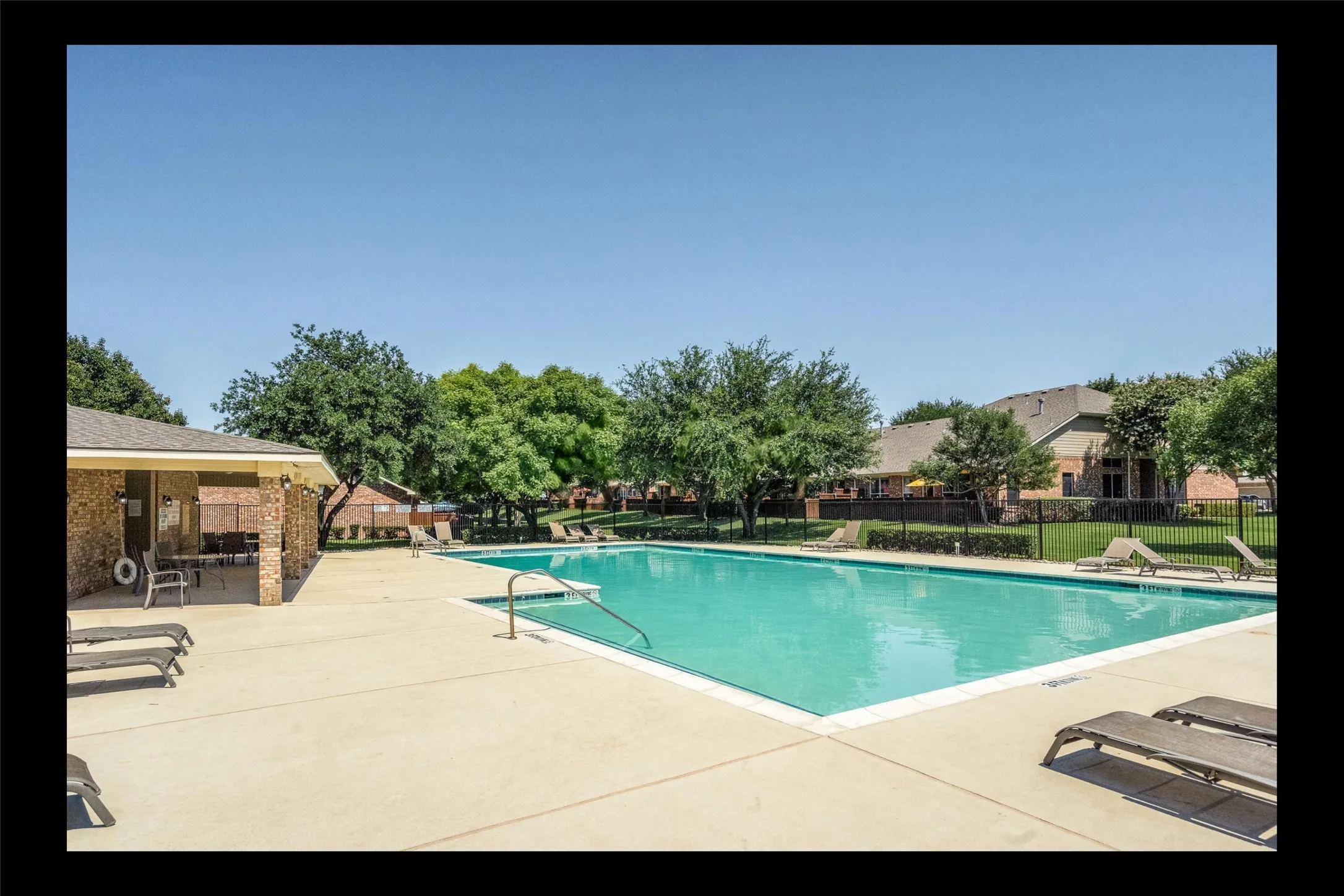 Expansive outdoor pool with a surrounding concrete deck, complemented by a brick-clad covered lounge area