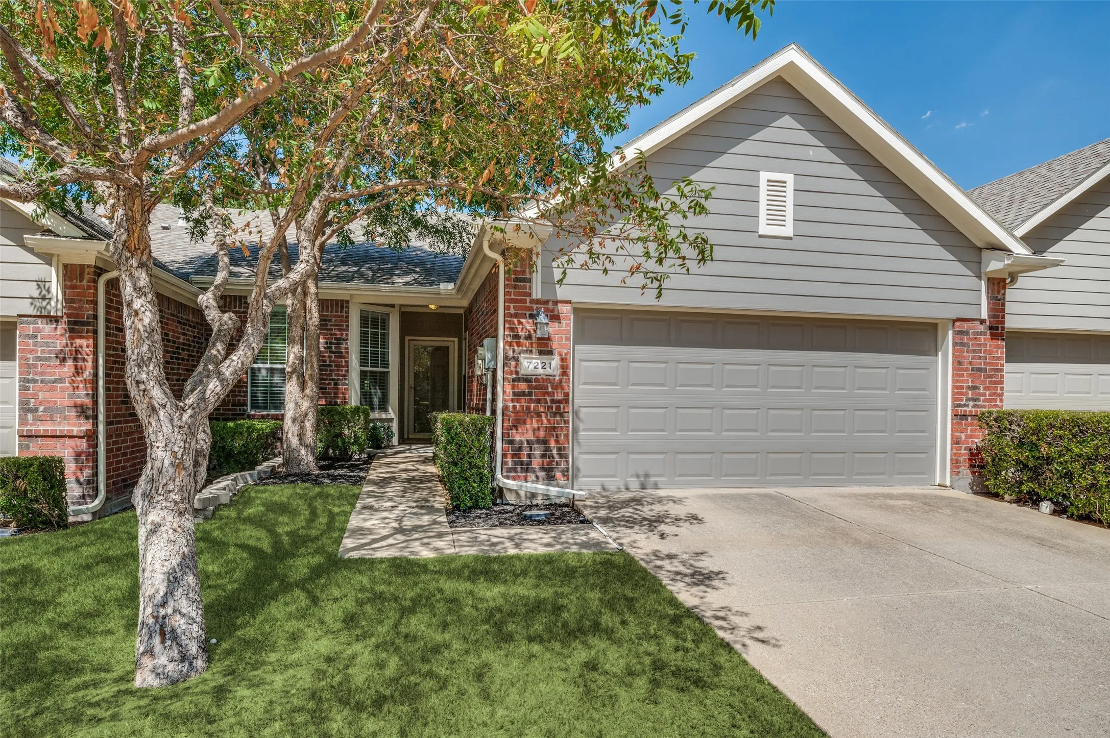 Brick and siding exterior with an attached garage, concrete driveway, and a front yard with mature trees