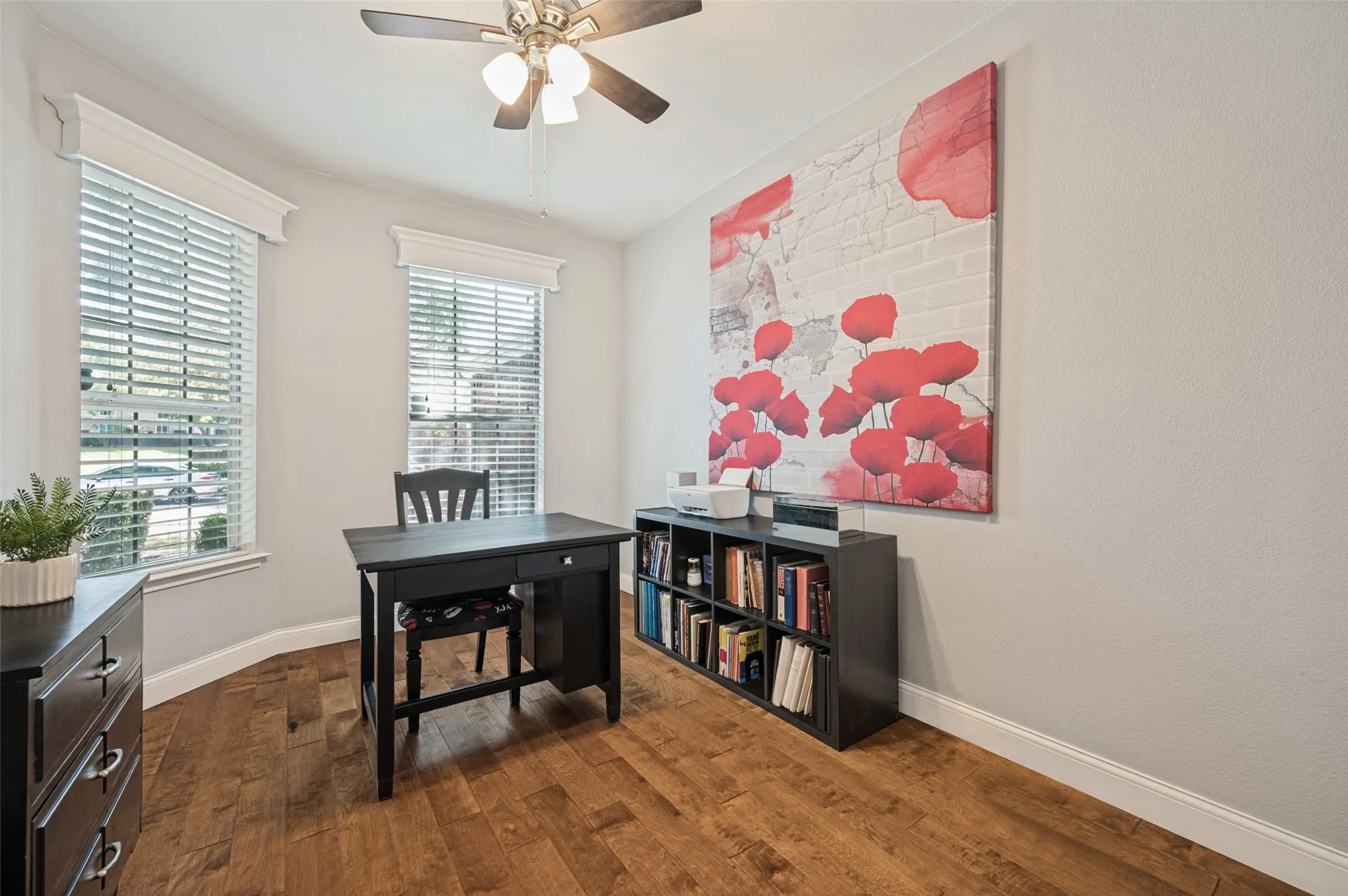 Hardwood flooring, two large windows with blinds, ceiling fan with integrated lighting, and a built-in bookshelf