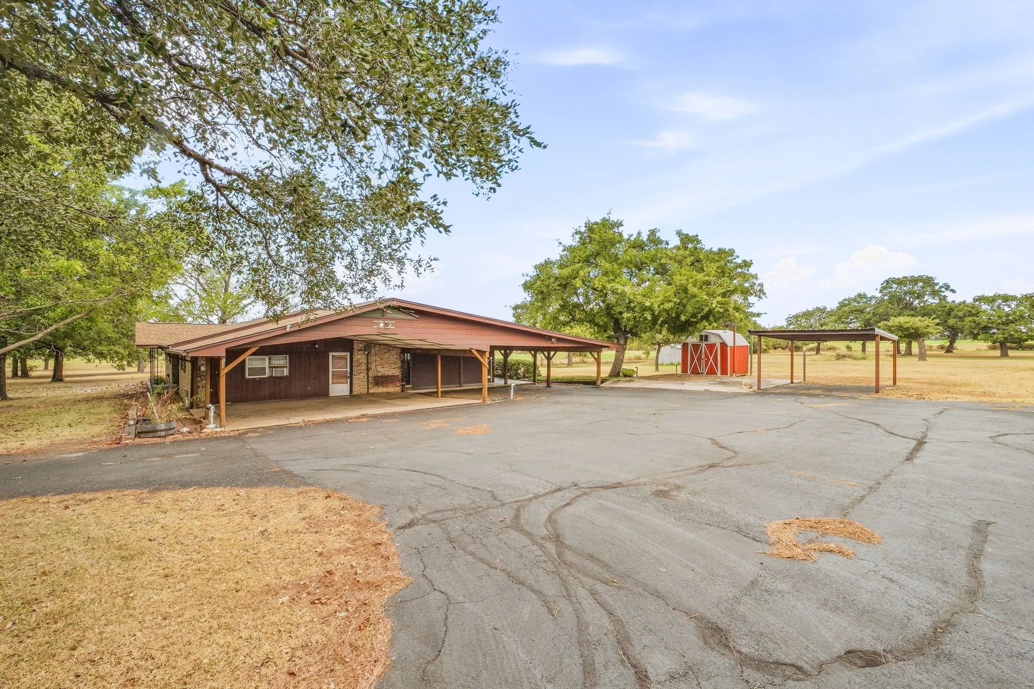 Expansive paved drive, attached carport, detached carport, and a red barn structure