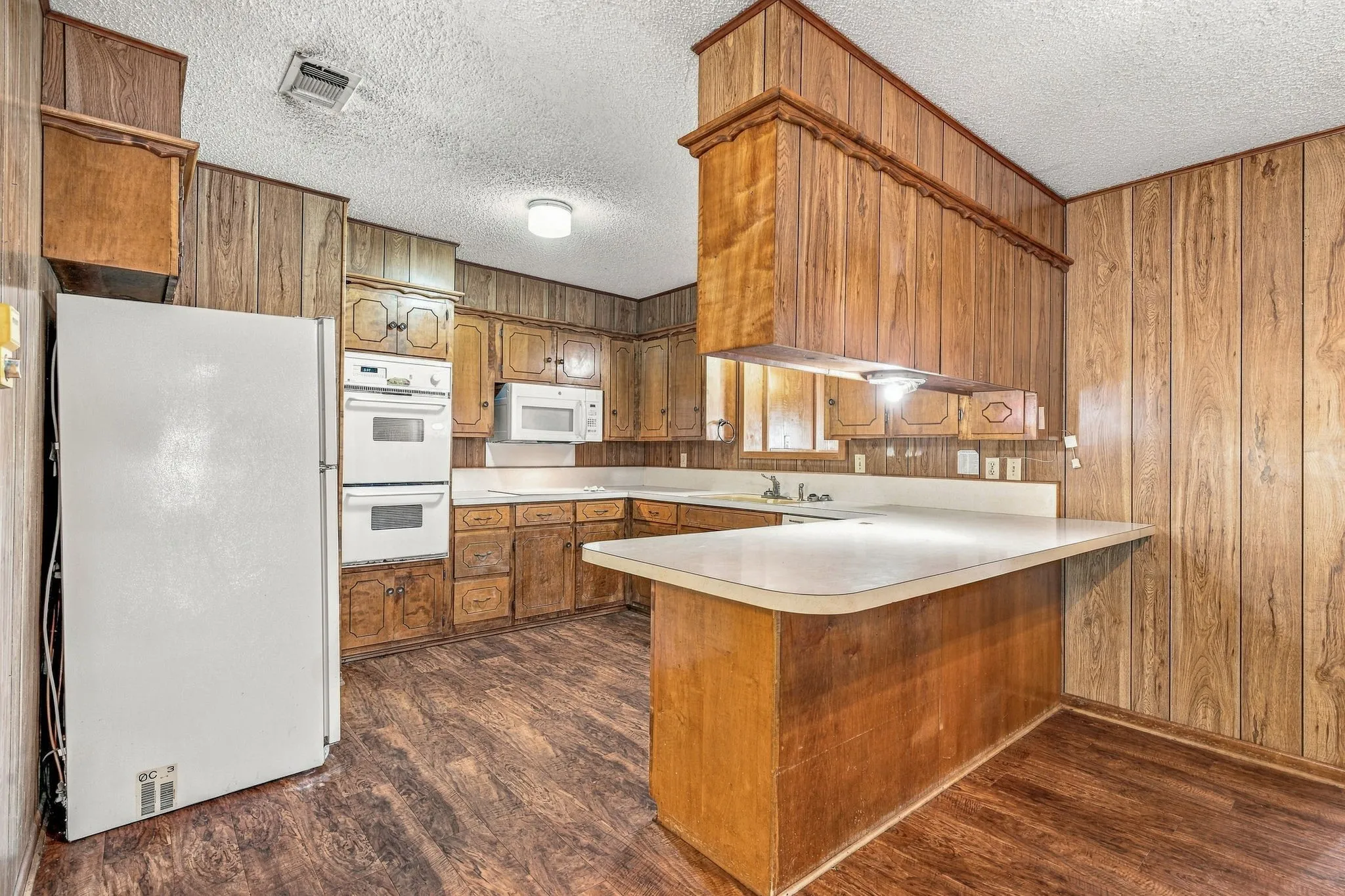 Kitchen featuring wood-finish paneling, wood-finish cabinetry, built-in double ovens, and a built-in microwave