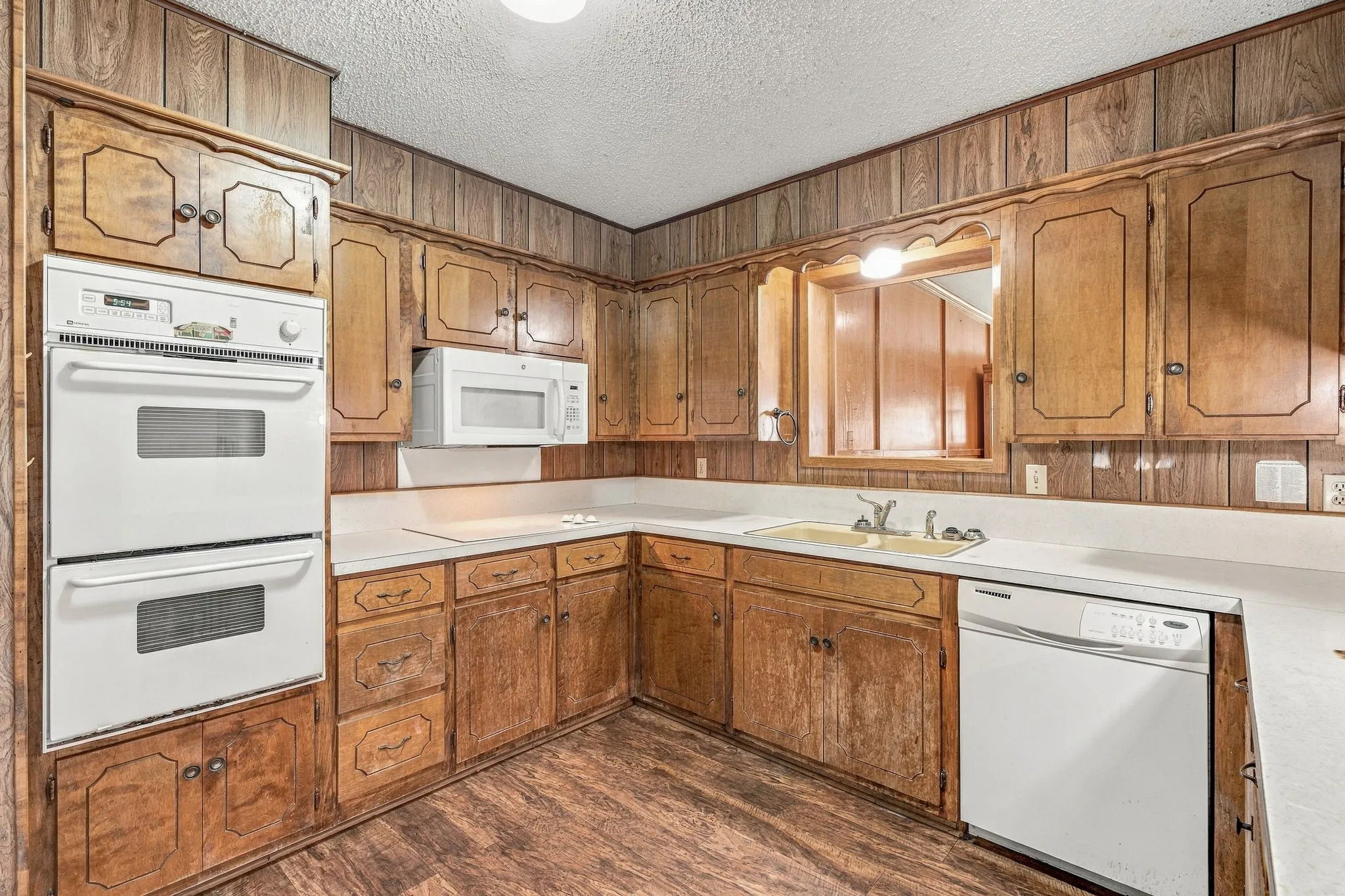 Wood-paneled kitchen with built-in double ovens, wood-finish flooring, ample cabinetry, white countertops, and a built-in microwave