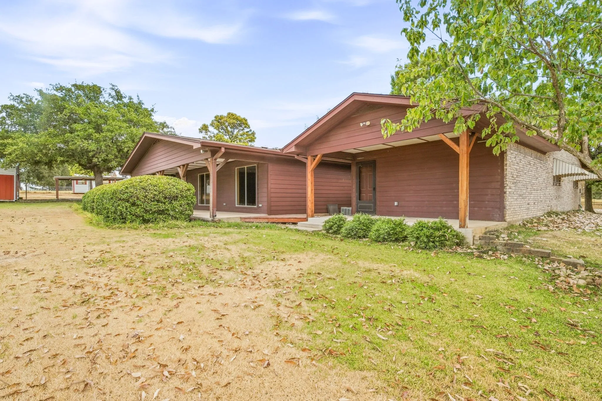 Exterior siding, covered porch, wood support beams, stone veneer accent, mature trees