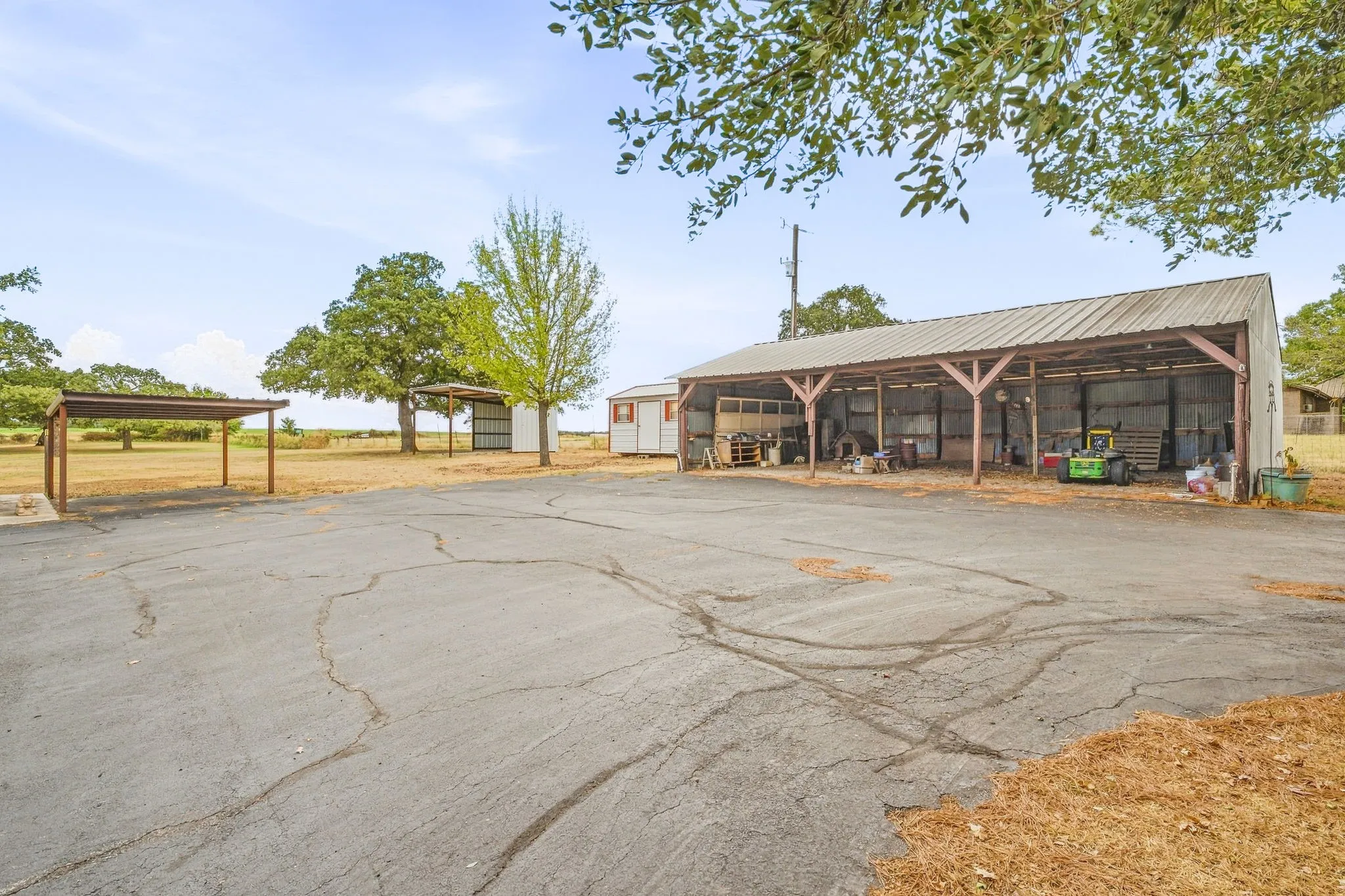 Expansive paved lot with multiple covered structures, including a large open-sided barn and two additional carports