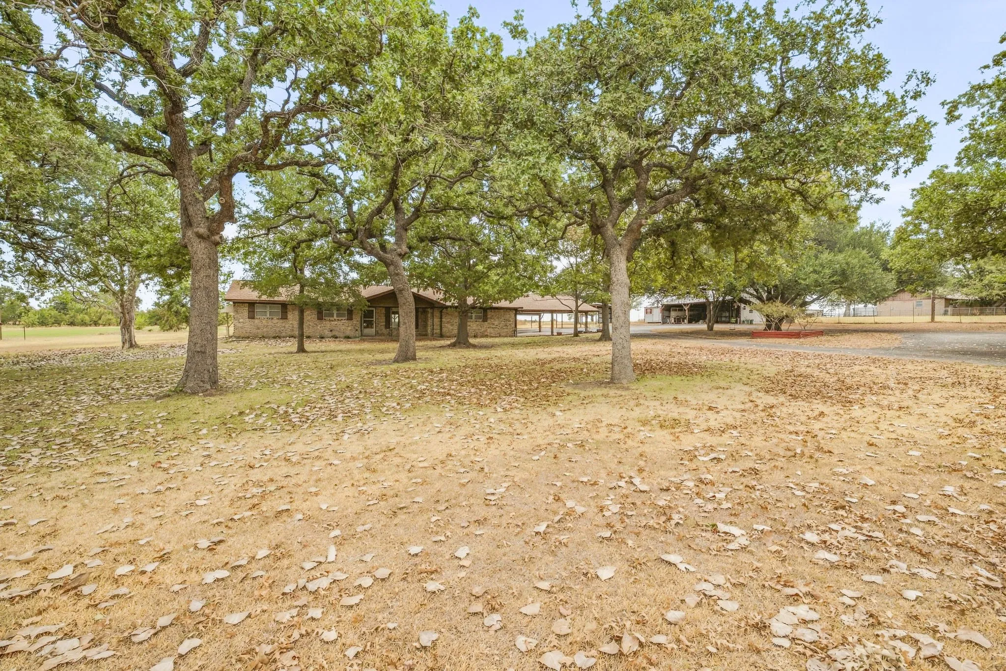 Expansive property featuring mature trees, a brick exterior residence, and a covered porch area