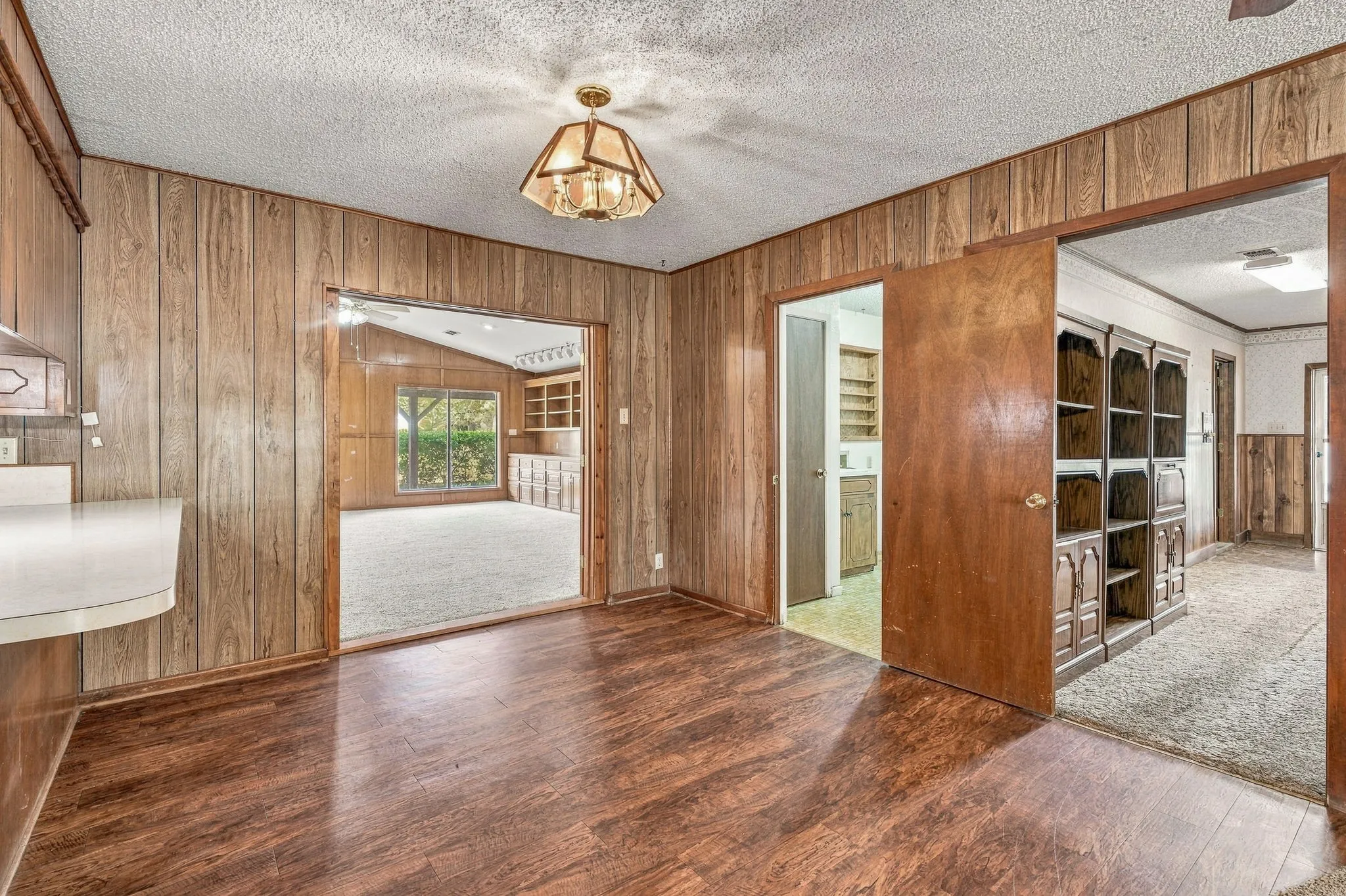 Wood-finish flooring, wood paneling, and an overhead decorative light fixture define this room, with a white countertop visible on the left