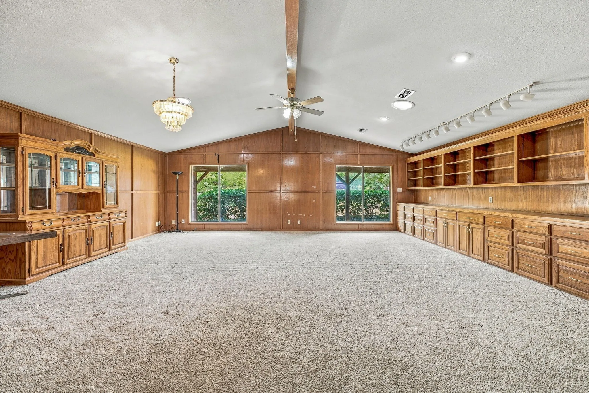 Vaulted ceiling with exposed beam, wood paneling, extensive built-in cabinetry, dual large windows, and recessed lighting