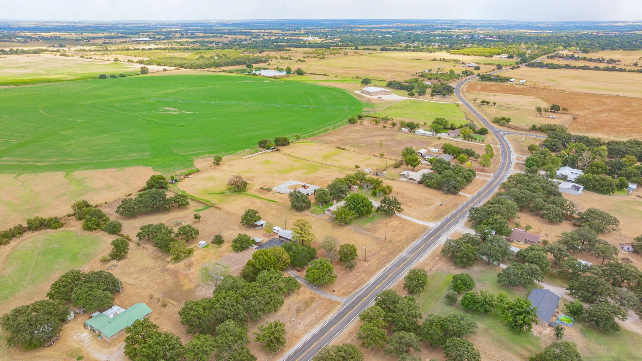 Expansive rural landscape featuring a paved road, scattered residences, mature trees, and agricultural fields