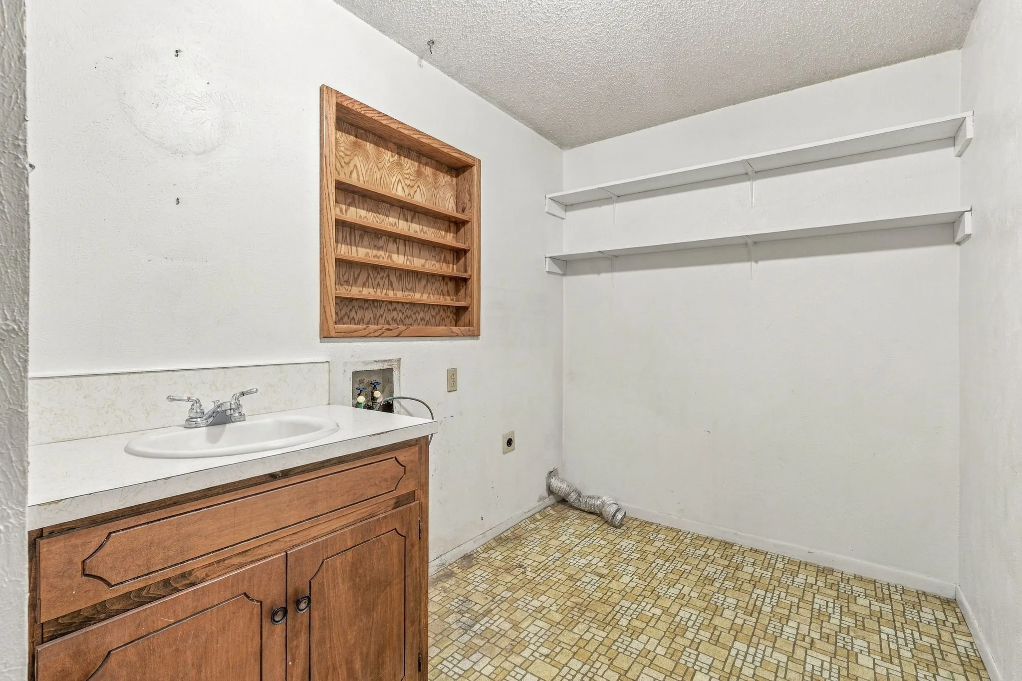 Utility space featuring a wood-finish vanity with an integrated sink, wall-mounted wood-finish shelving, and overhead white shelving