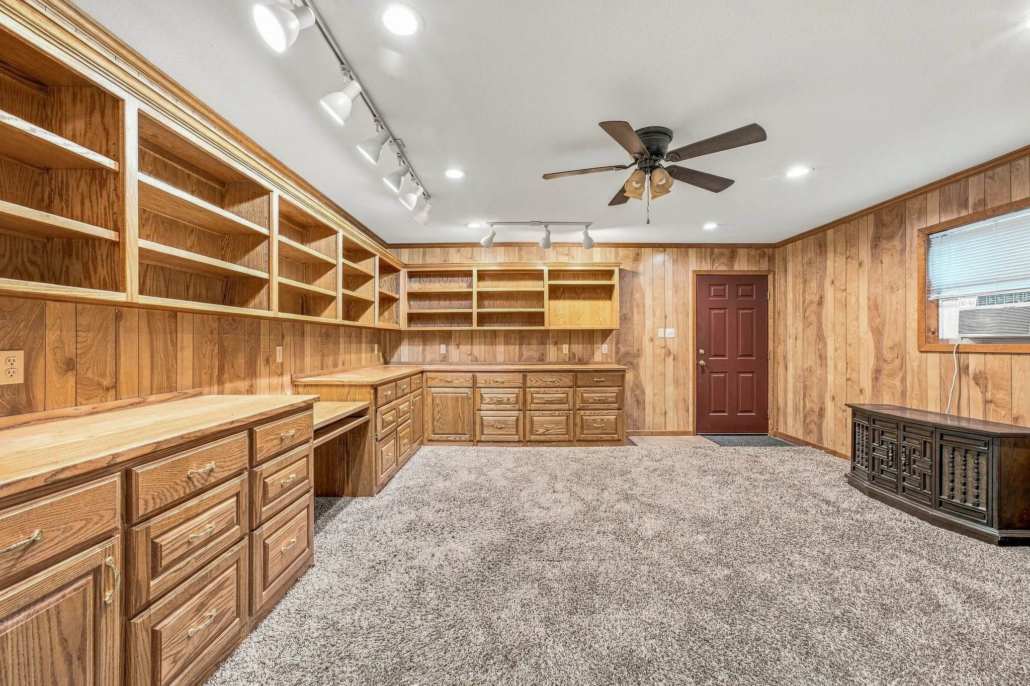 Wood-paneled walls with extensive built-in shelving, integrated desk space, and a ceiling fan