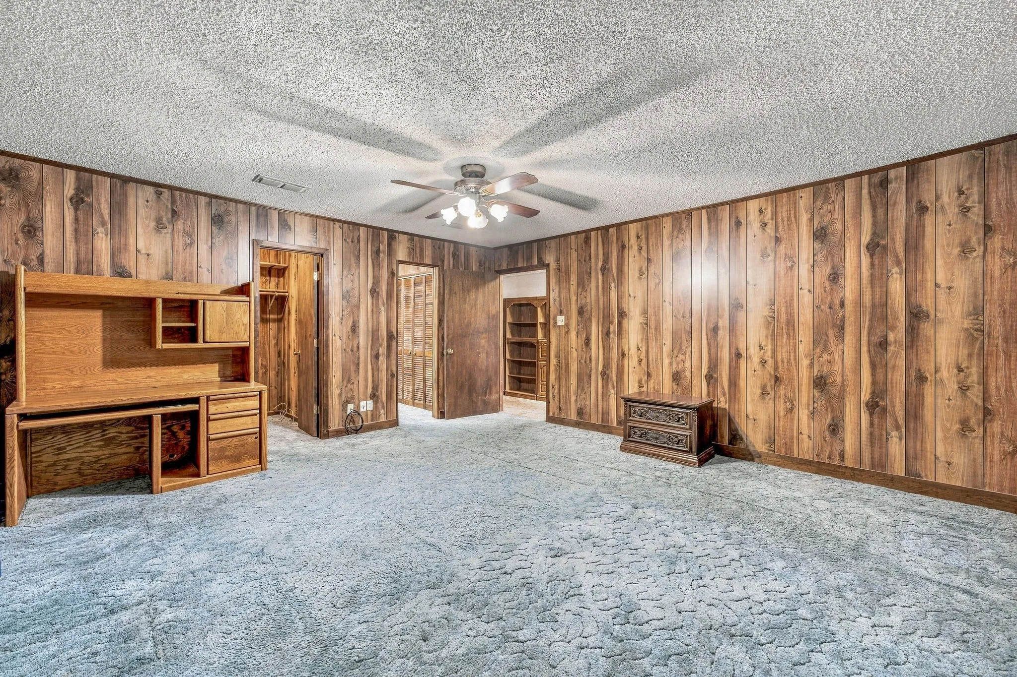 Wood-panel accent walls, patterned carpeting, and a ceiling fan with integrated lighting