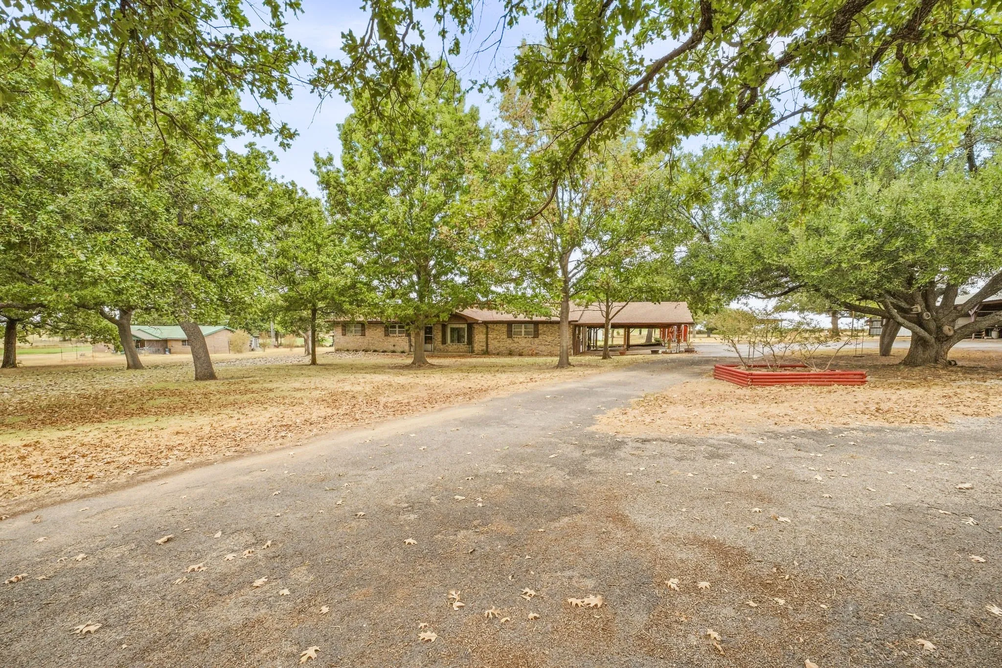 Paved driveway leading to a brick-clad residence with a covered front porch, surrounded by mature trees and natural landscaping