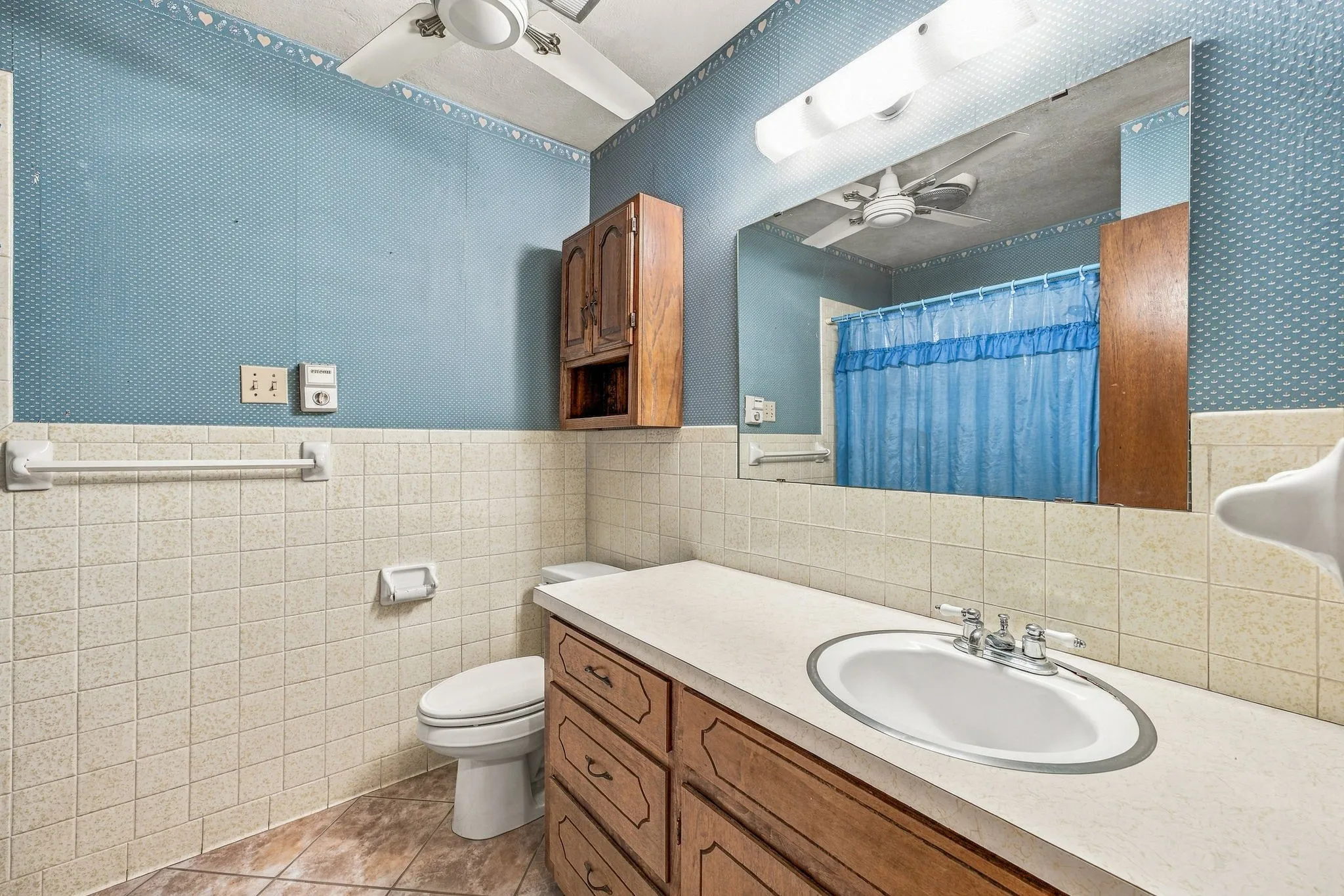 Built-in wood-finish cabinetry, vanity with integrated sink, ceramic tile walls, and ceiling fan