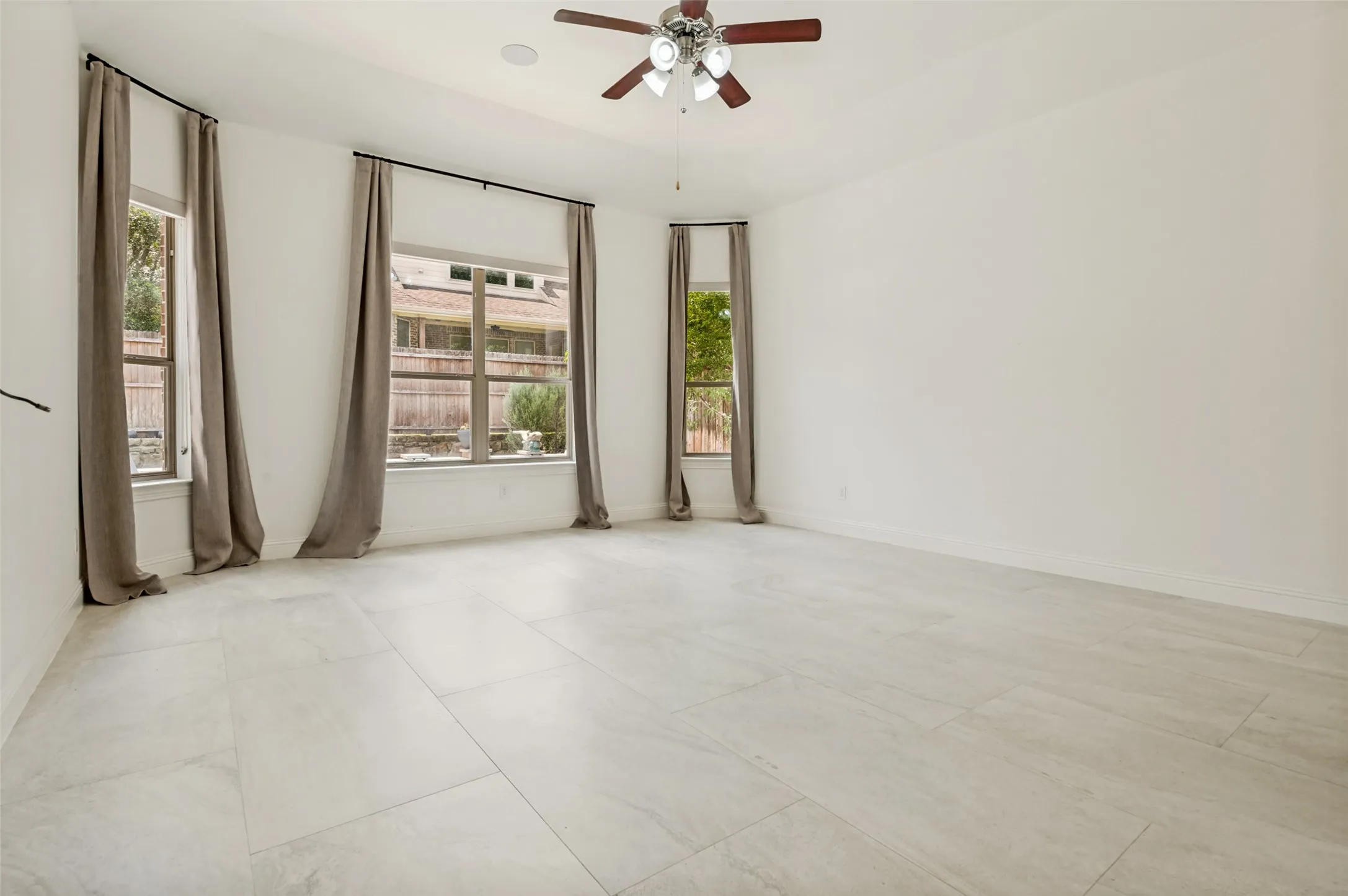 Spacious room featuring light-toned tile flooring, multiple windows with neutral drapery, a ceiling fan with light fixture, and recessed lighting