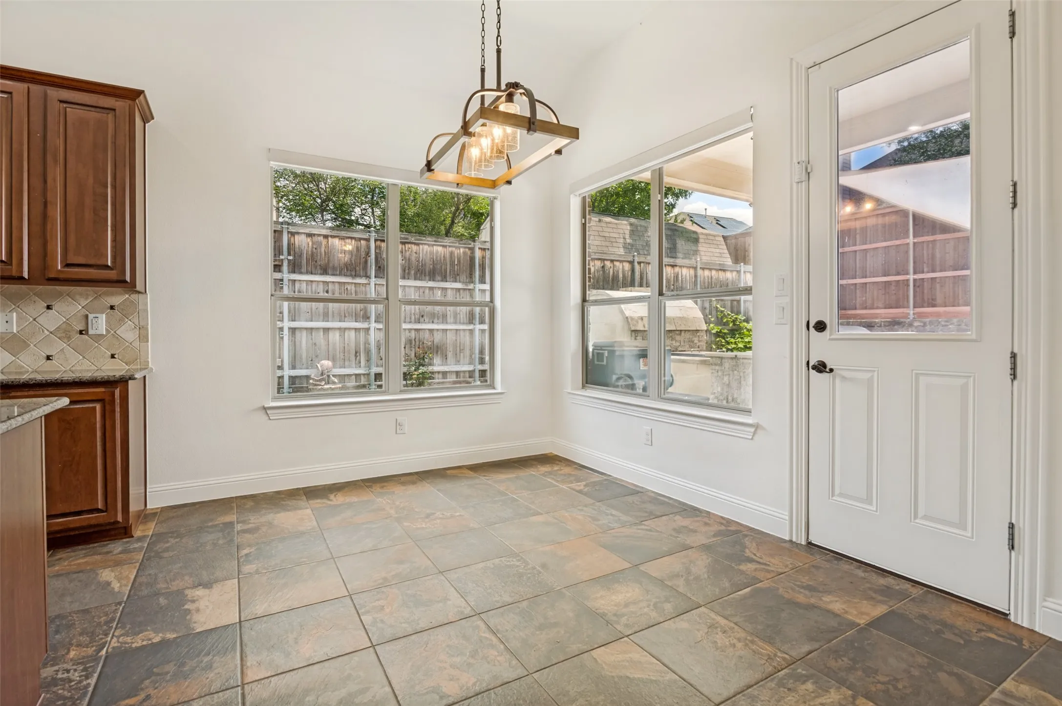 Dining area featuring large tile flooring, a vaulted ceiling with an industrial-style chandelier, and multiple windows providing natural illumination