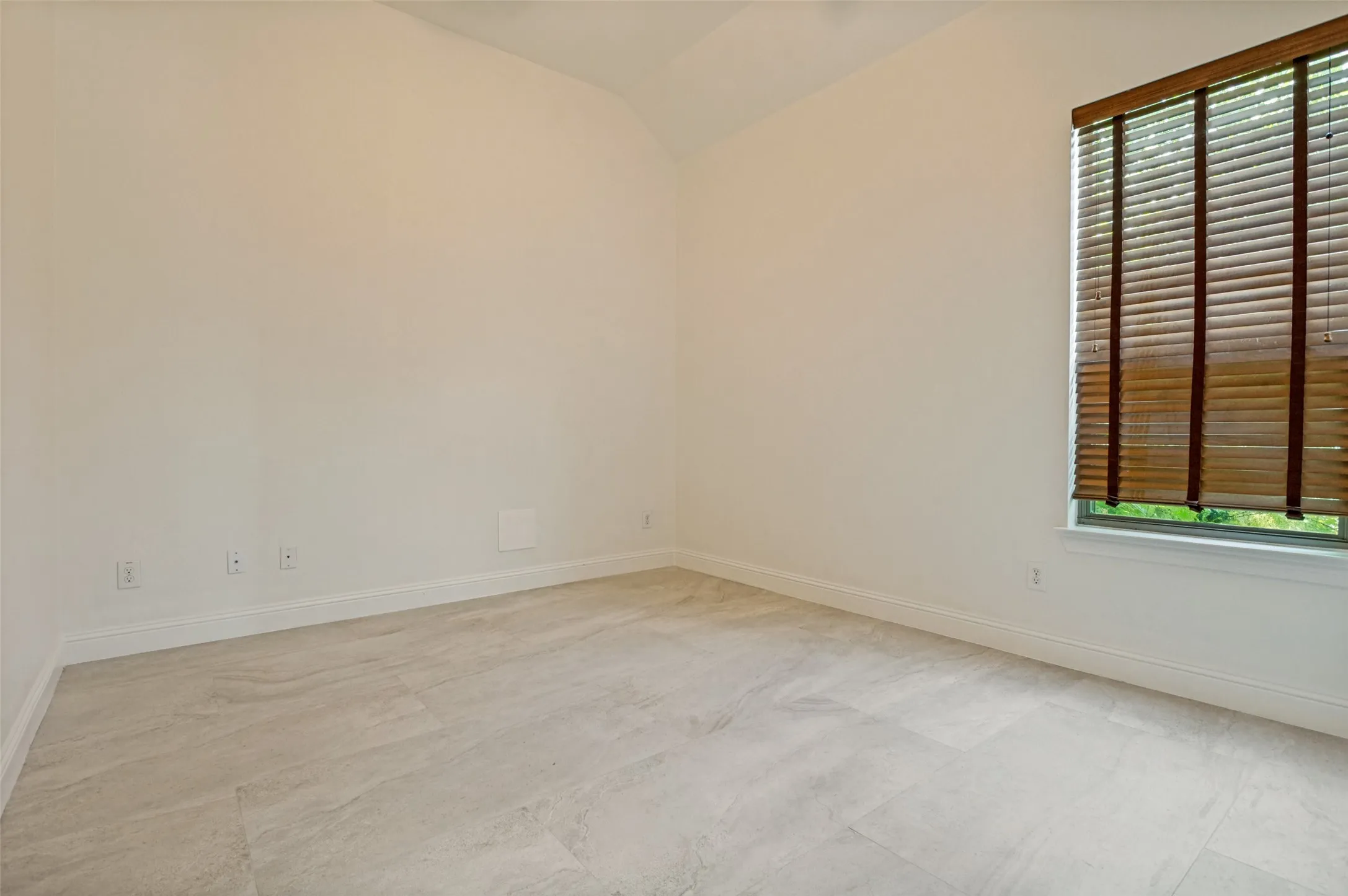 Light-filled interior space featuring a single window with wooden blinds, light-toned tile flooring, and white baseboards