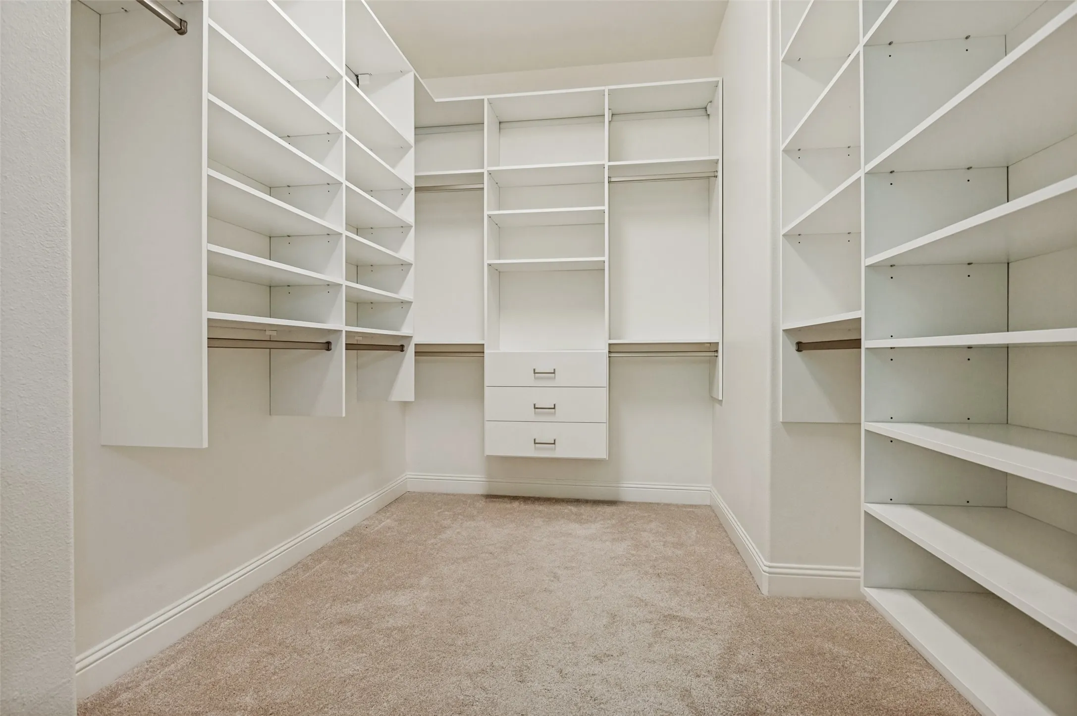 Walk-in closet featuring built-in white shelving, hanging rods, and integrated drawers