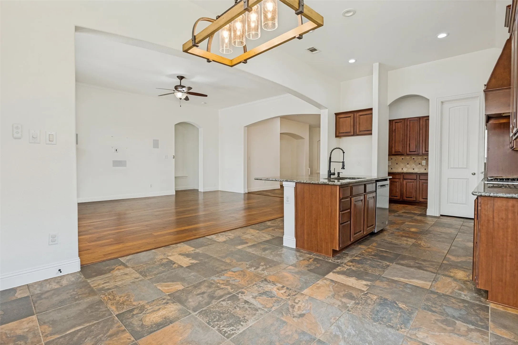 Kitchen featuring an island with a built-in sink, granite countertops, wood cabinetry, and stainless steel appliances