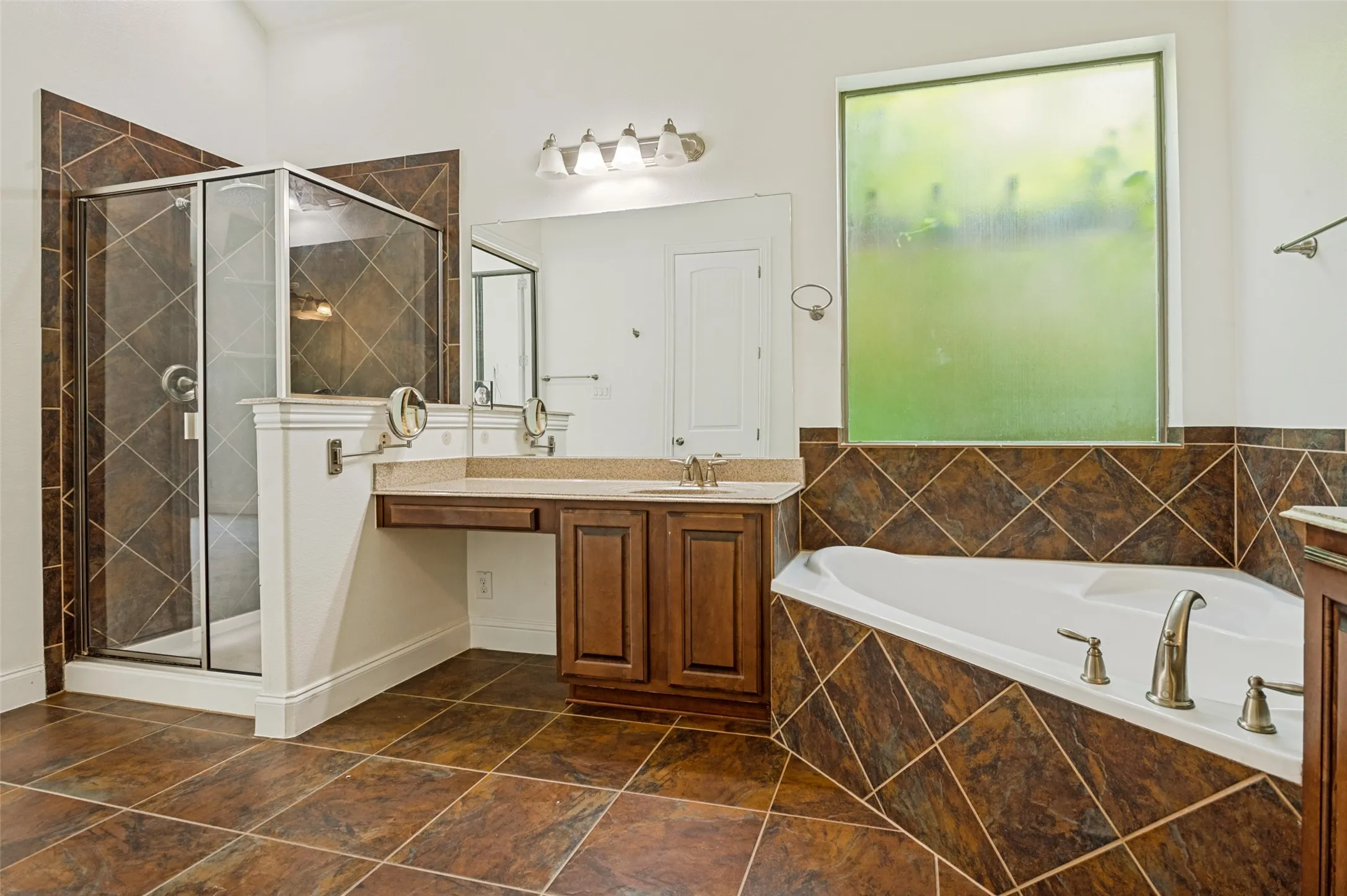 Bathroom featuring a corner soaking tub, a separate glass-enclosed shower, a dual-sink vanity with a makeup counter, and a large privacy window