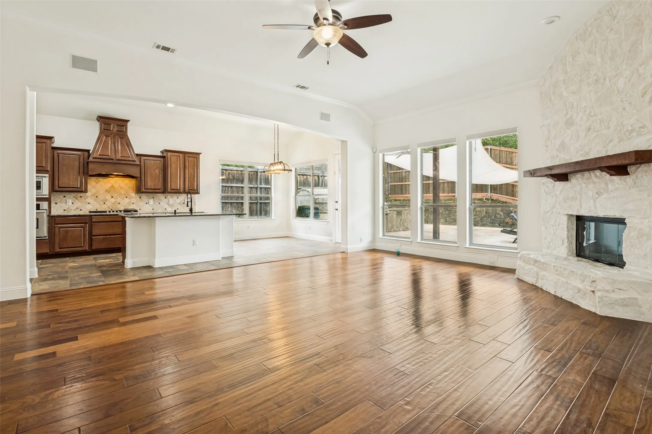 Spacious open-concept living area featuring wood-finish flooring and a stone fireplace with a substantial wood mantel