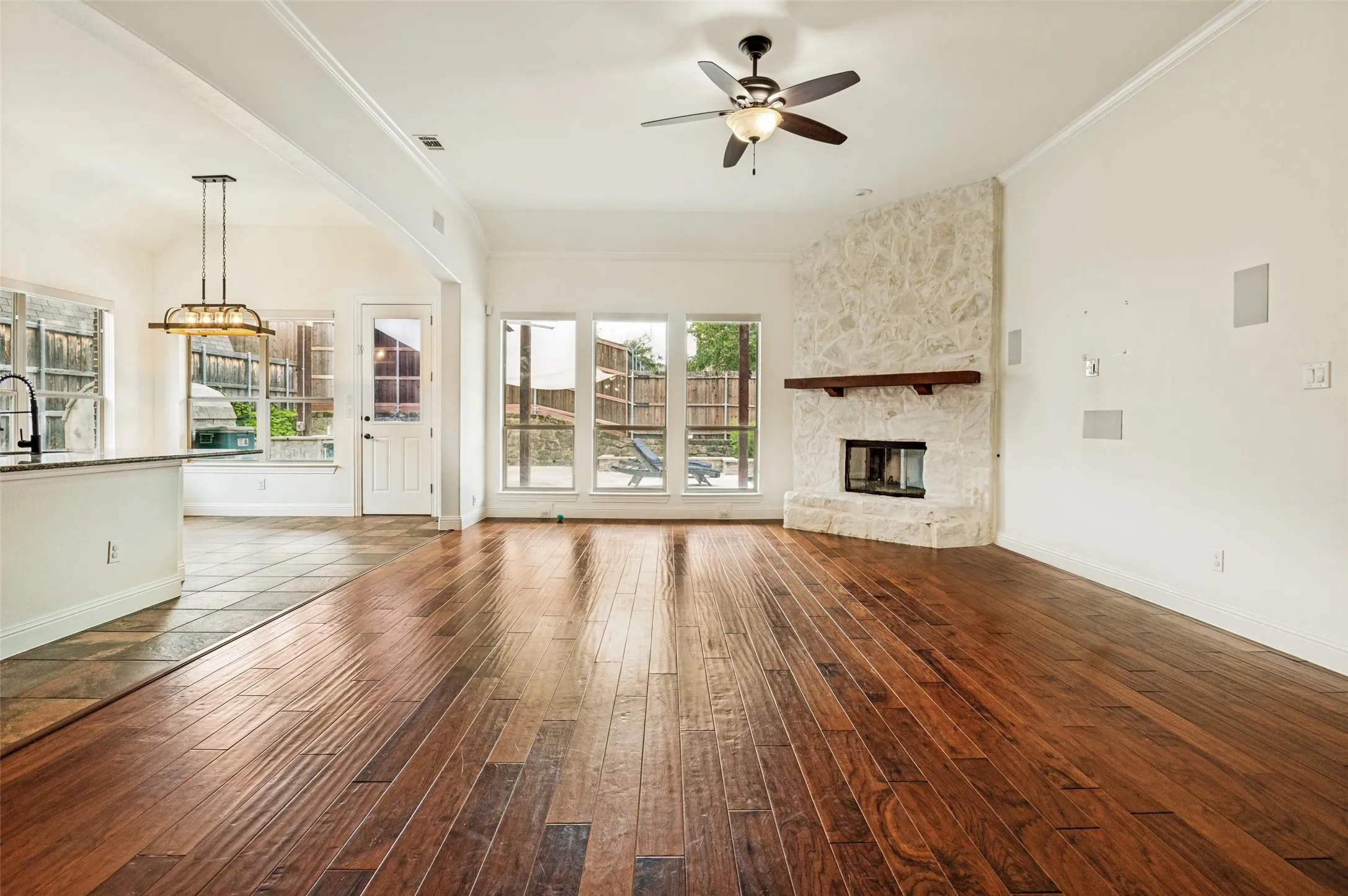 Spacious living area featuring wood-finish flooring, a stone fireplace with a substantial wood mantel, and multiple large windows