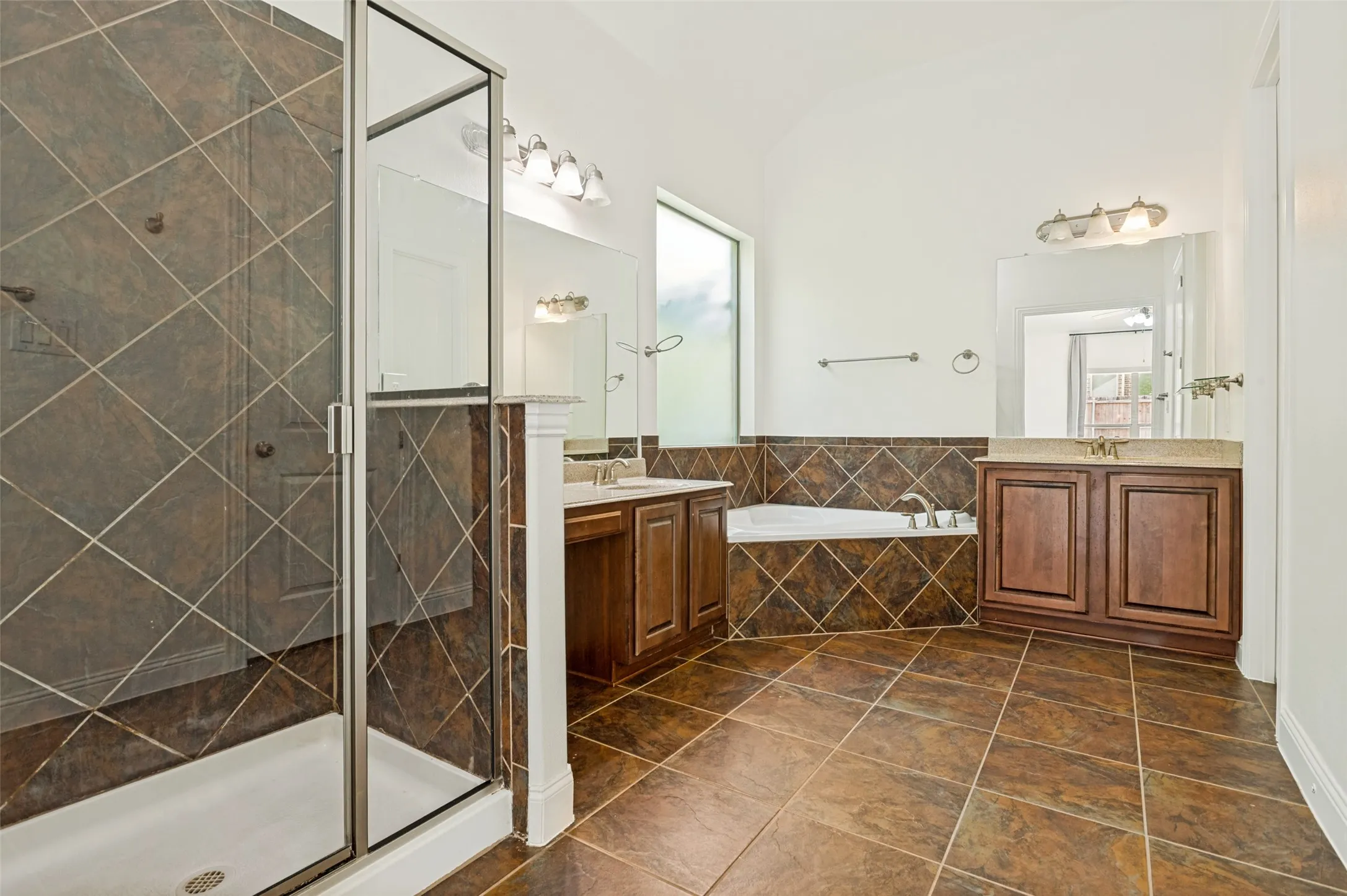 Spacious bathroom featuring a glass-enclosed shower, built-in soaking tub, dual vanity with wood cabinetry, and extensive diagonal tile work