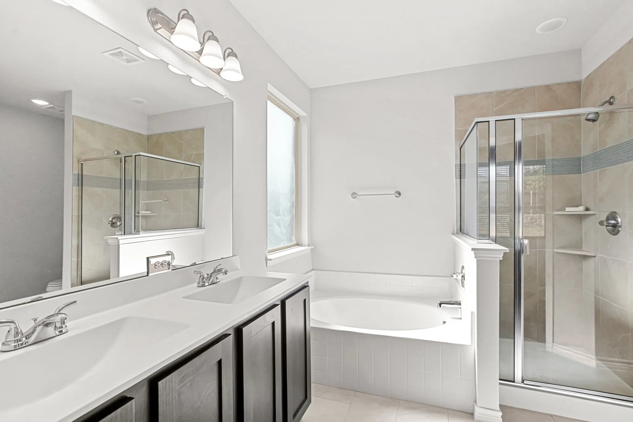 Dual vanity with integrated sinks, built-in soaking tub, glass-enclosed shower, tiled shower surround, and a large wall mirror