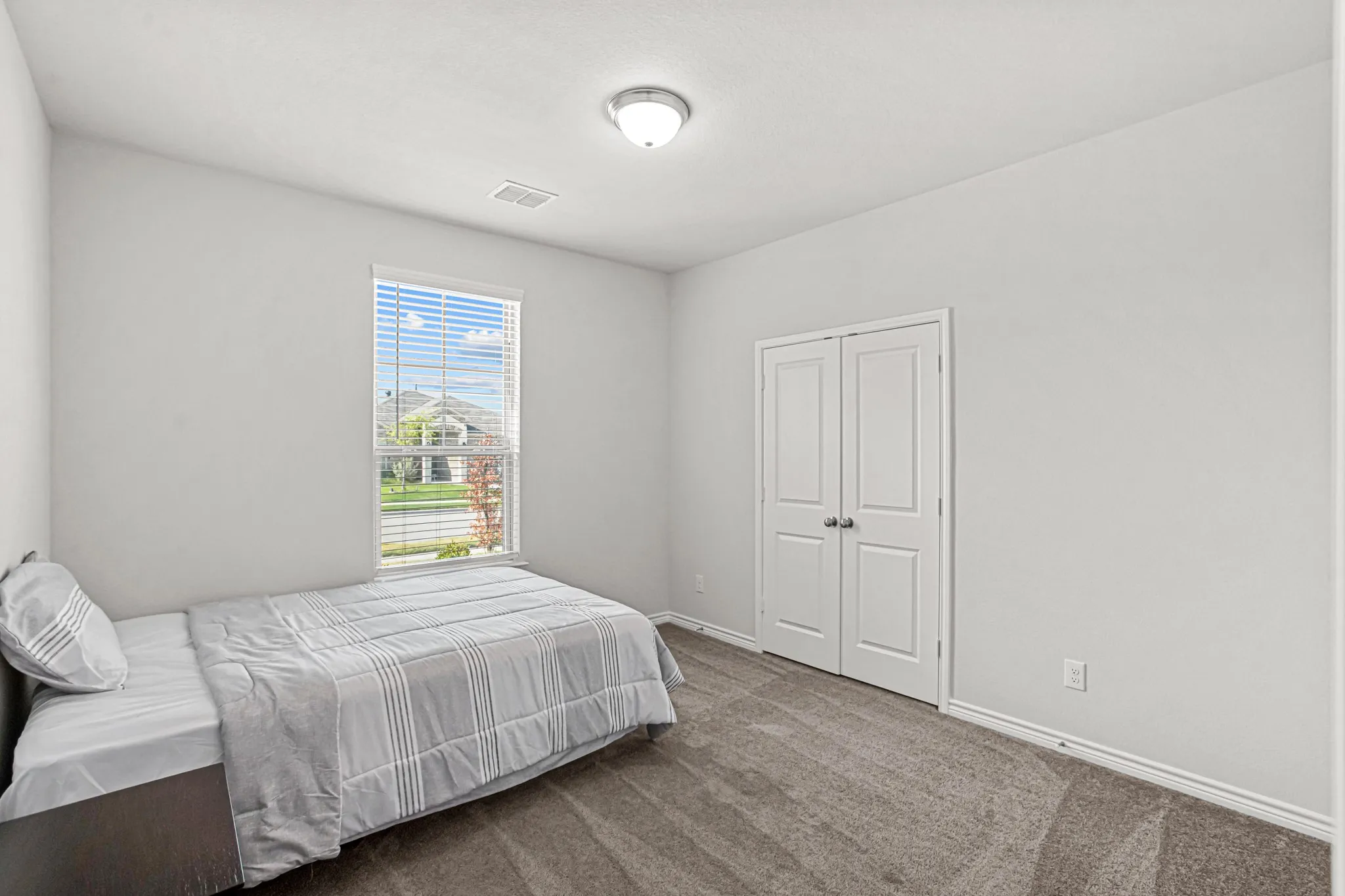 Neutral wall paint, carpet flooring, a window with blinds, and a double-door closet