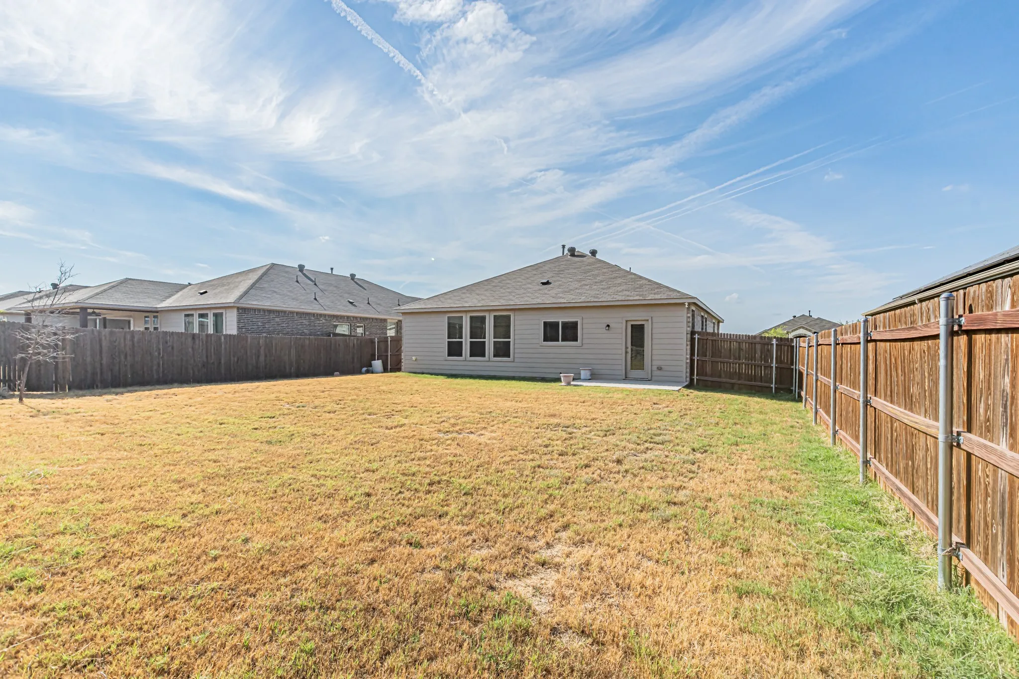 Expansive backyard with a wood privacy fence, concrete patio, and rear exterior access