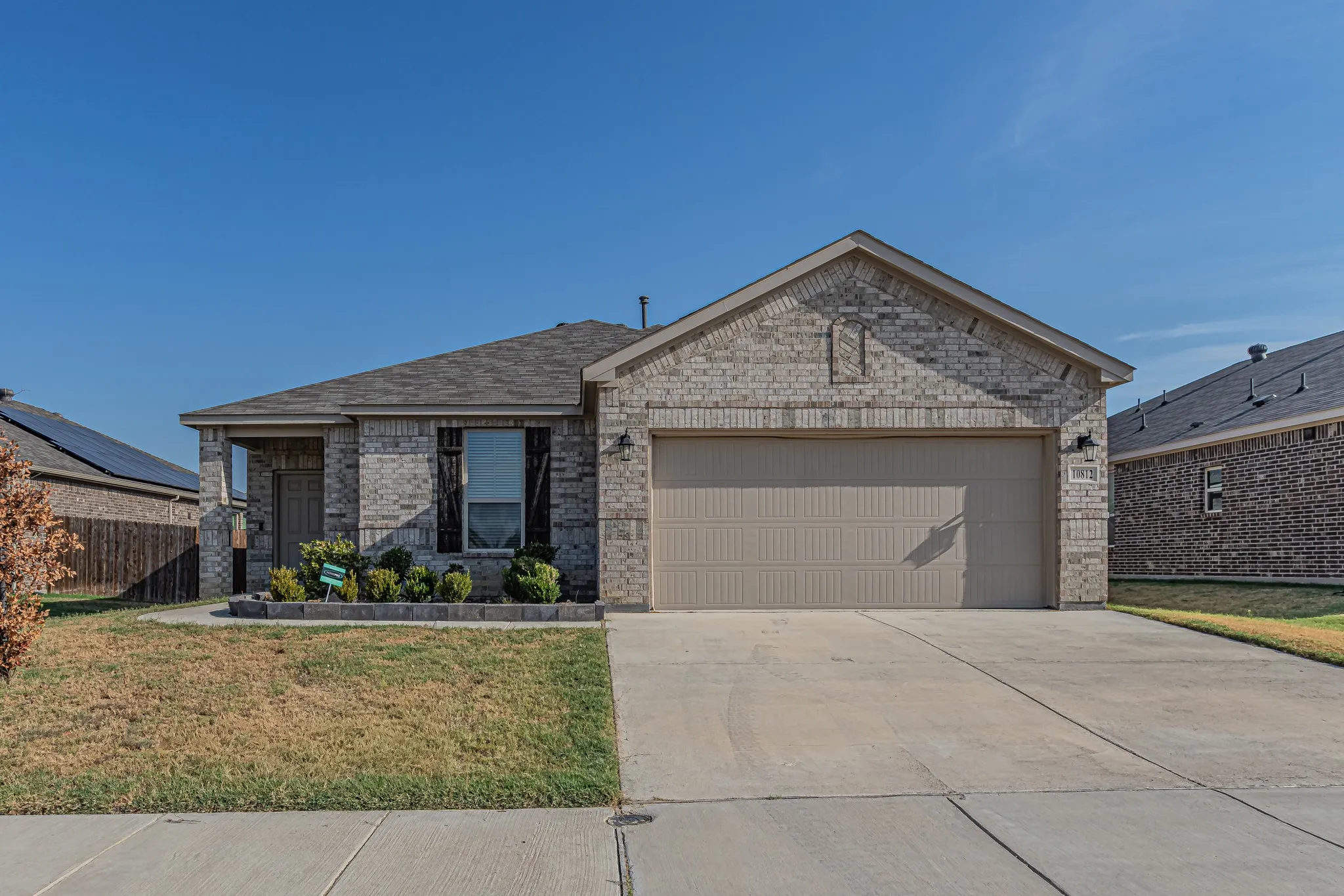 Brick facade, attached two-car garage, covered porch entry, and front landscaping