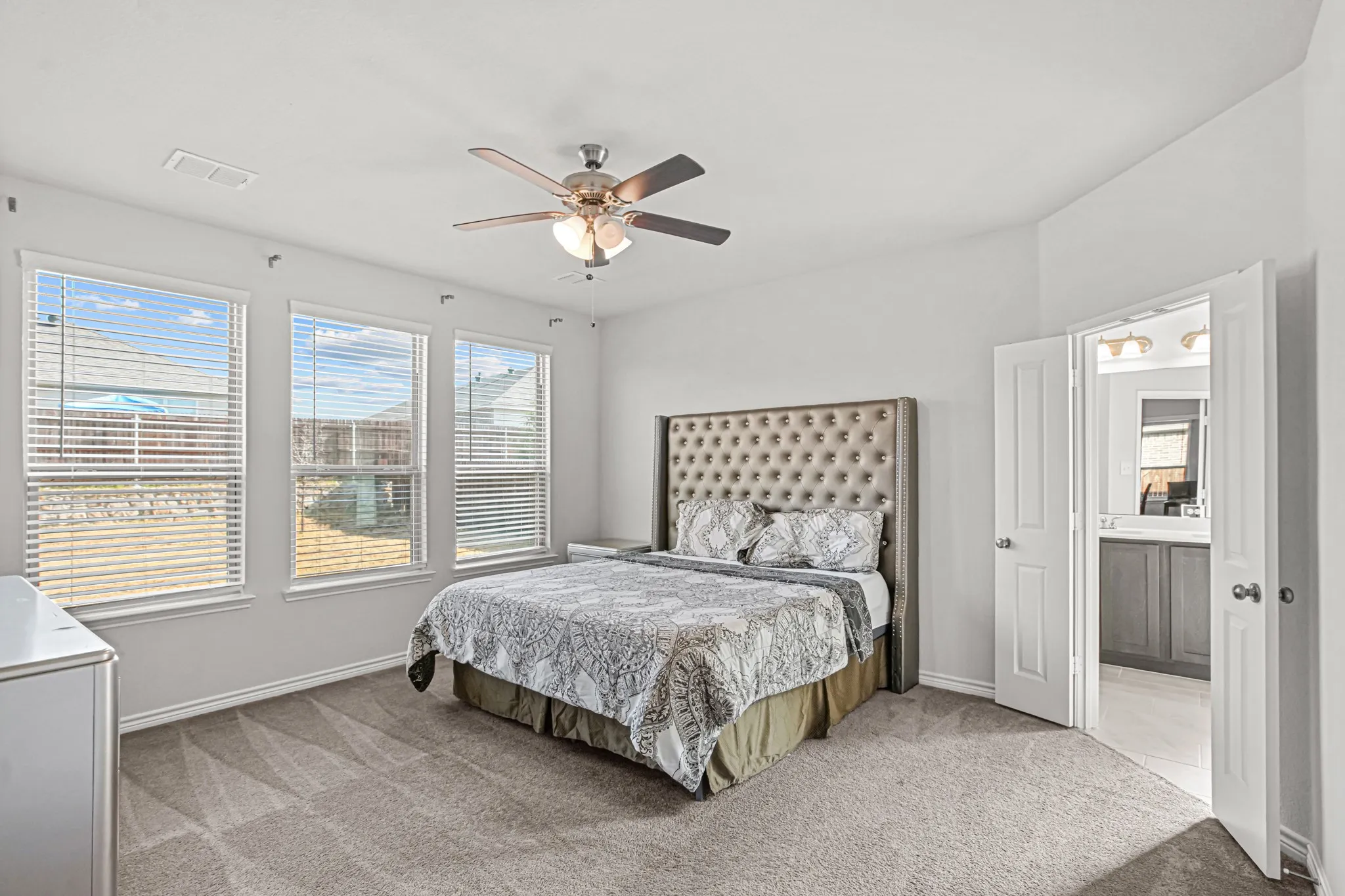 Carpeted room with three windows, a ceiling fan, and a neutral color palette