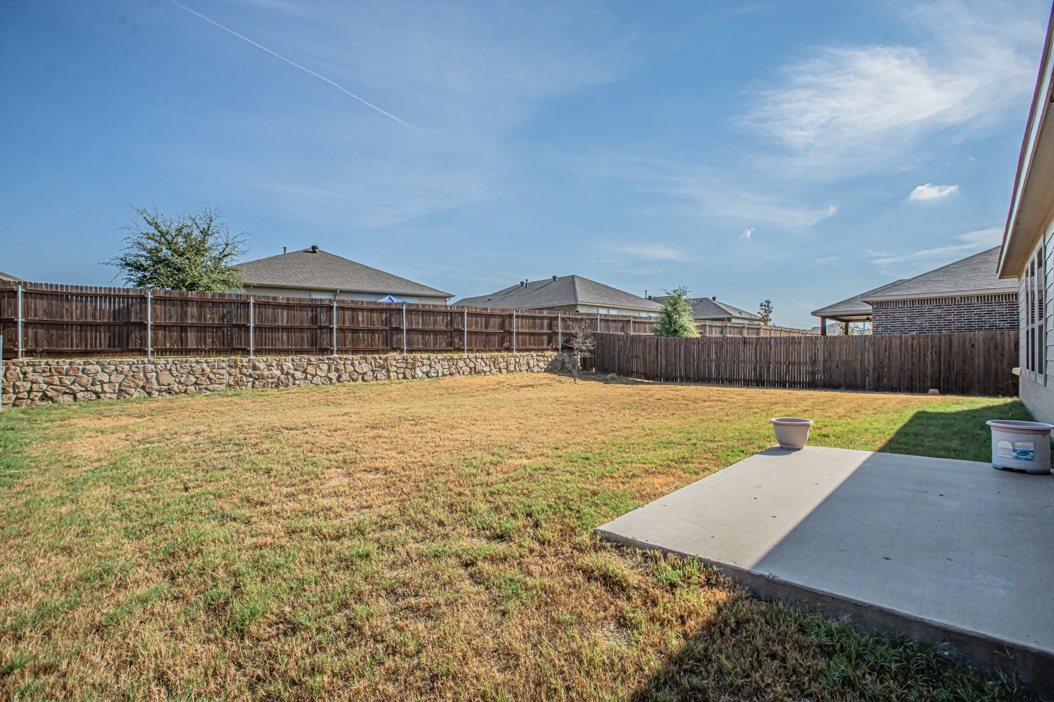 Expansive backyard with a flat lawn, wood privacy fence, and a stone retaining wall