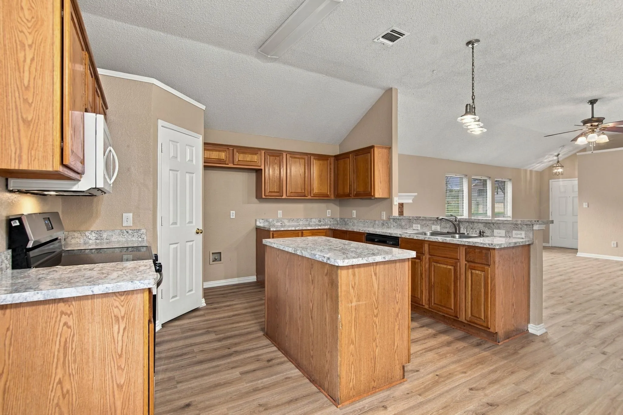Kitchen featuring wood-finish cabinetry, granite-style countertops, an island, stainless steel appliances, and wood-finish flooring