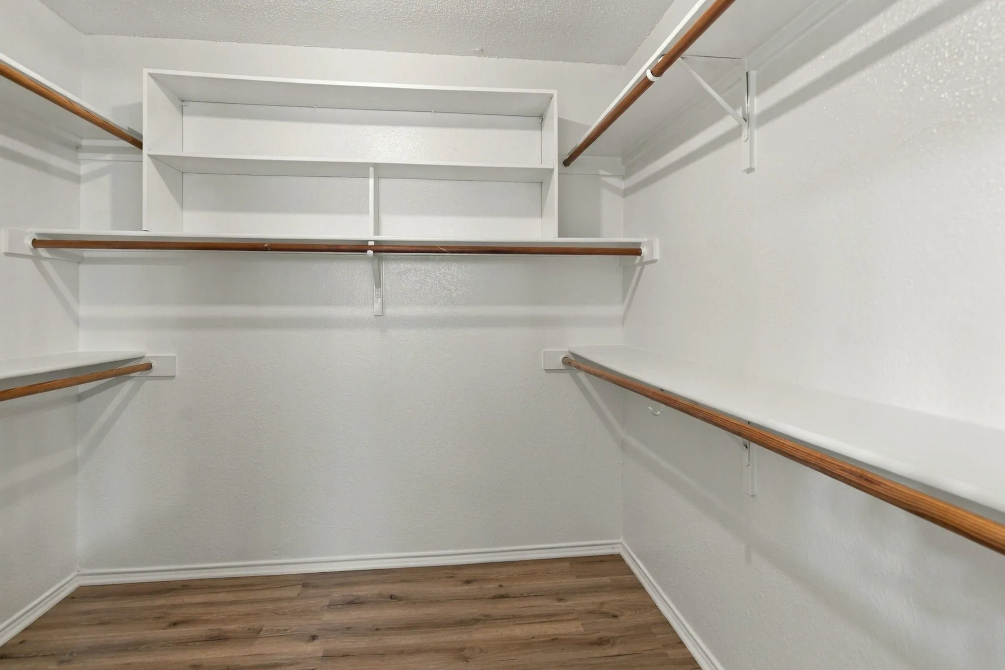 Walk-in closet with built-in shelving, multiple hanging rods, and wood-finish flooring