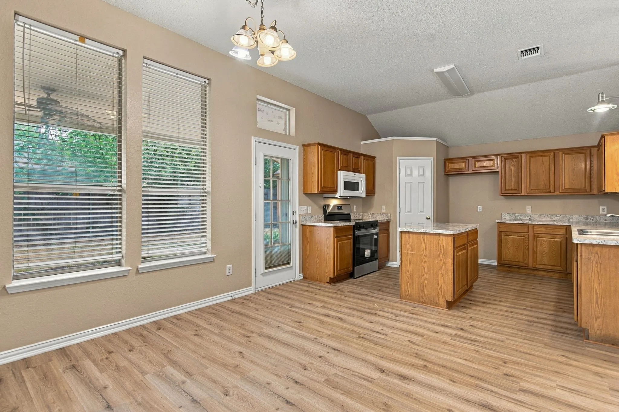 Kitchen featuring wood-finish flooring, a central island, light-toned countertops, wood cabinetry, and stainless steel appliances
