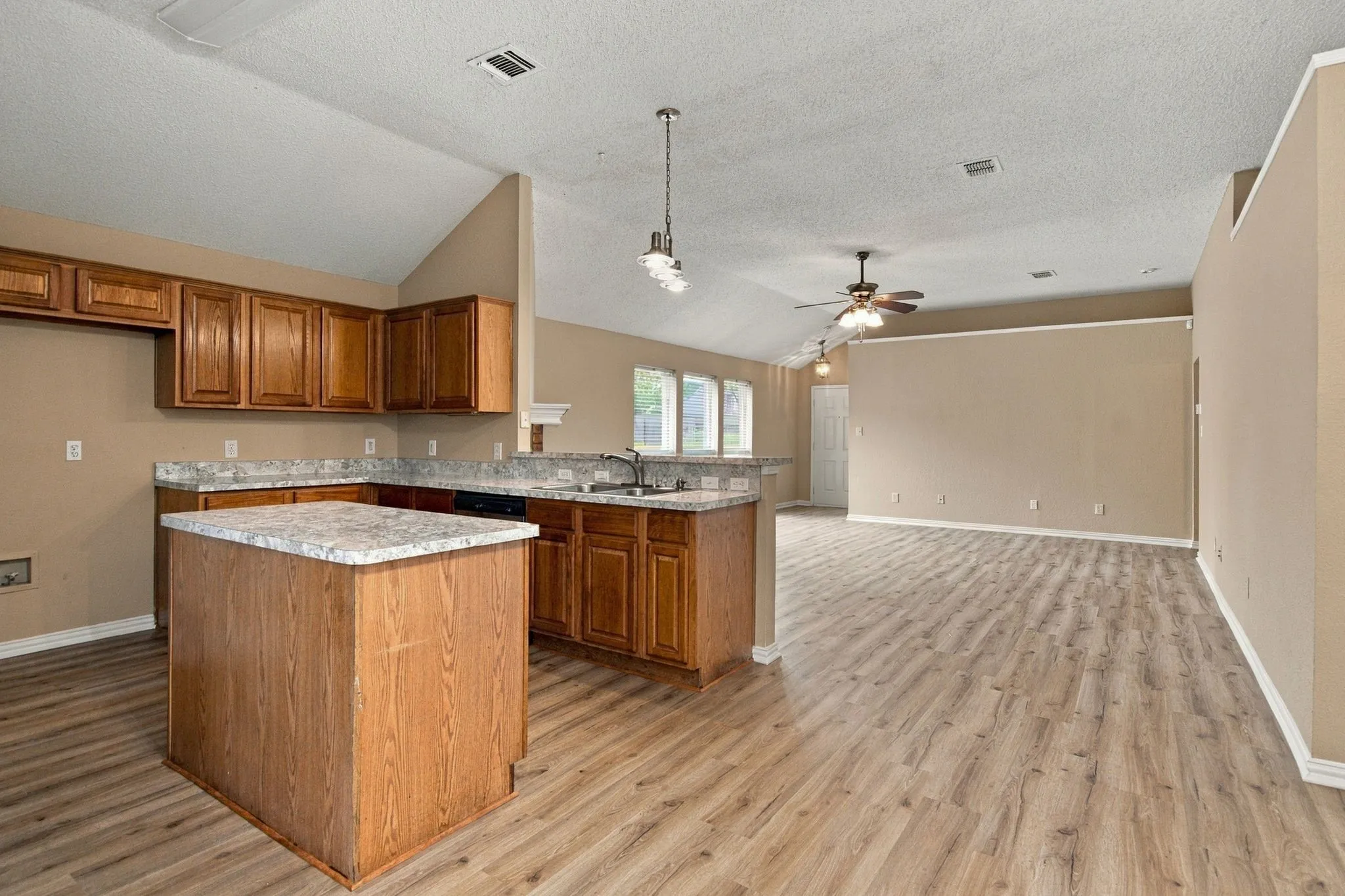 Kitchen island with counter seating, wood-finish cabinetry, light-toned countertops, wood-finish flooring, and vaulted ceiling